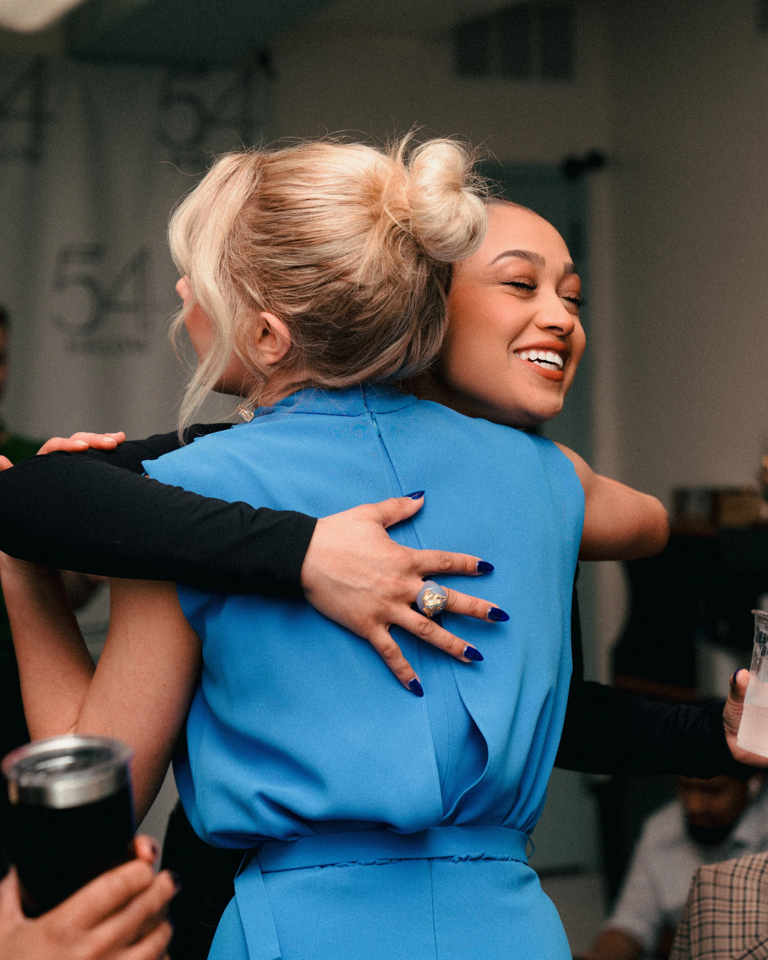 Two women hugging at a social gathering, smiling and happy.
