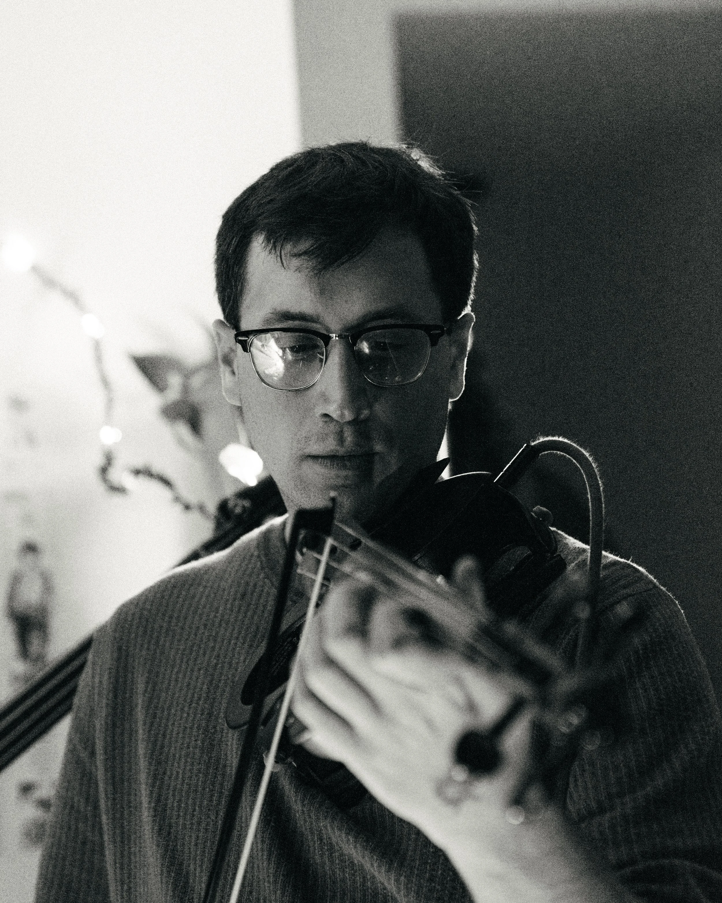 A man with glasses looking at a camera or smartphone in a black-and-white photo, with a blurred background.