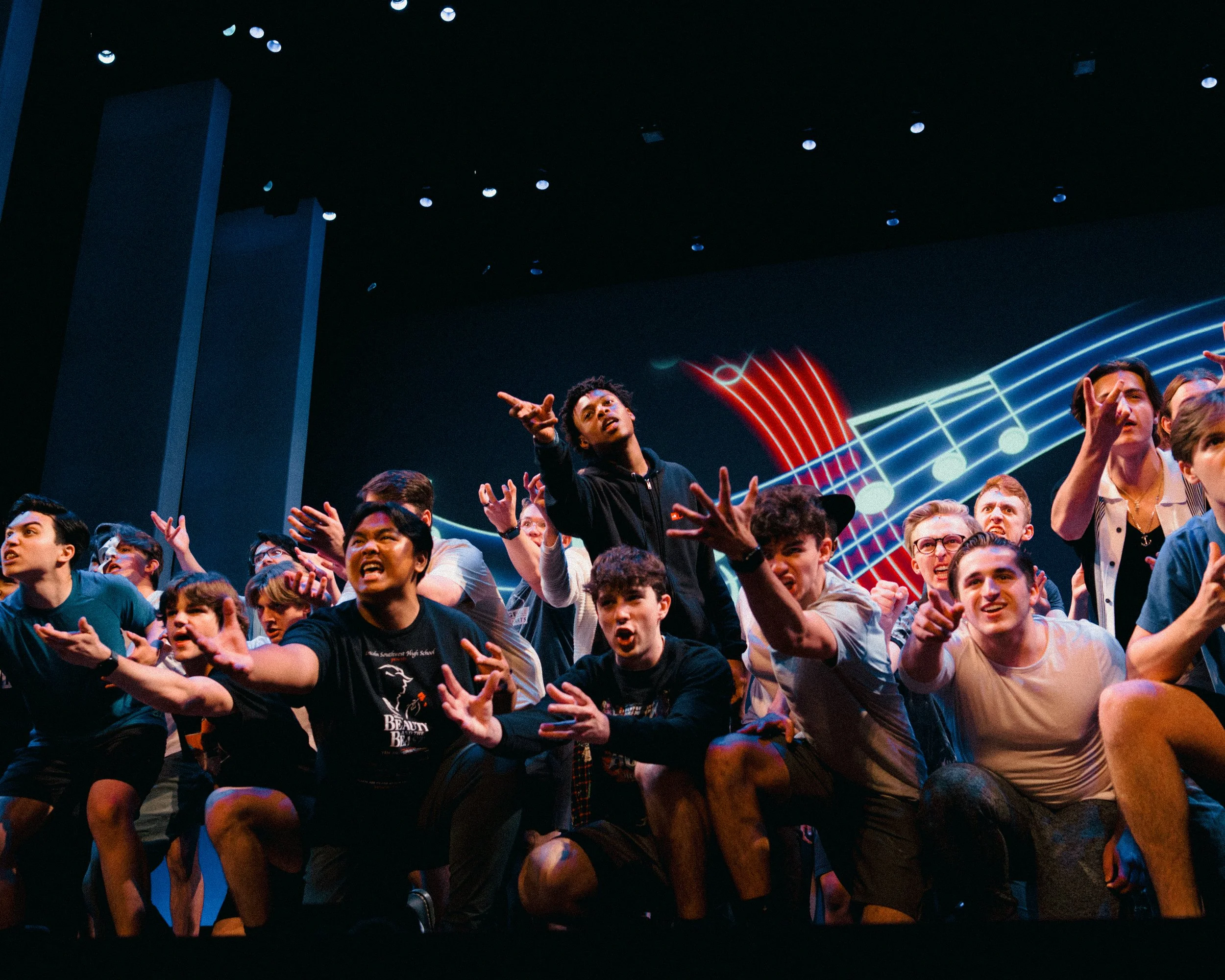 A group of diverse young people on stage, singing and dancing with animated musical notes and staff in the background.