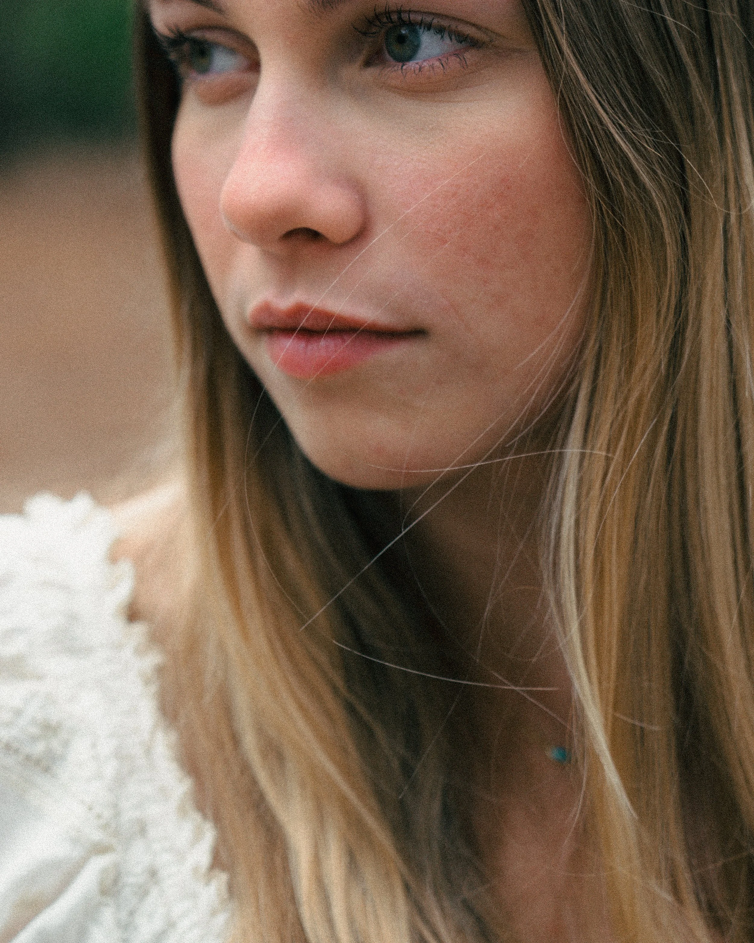 Close-up of a young woman's face with blond hair and blue eyes, looking to the side.