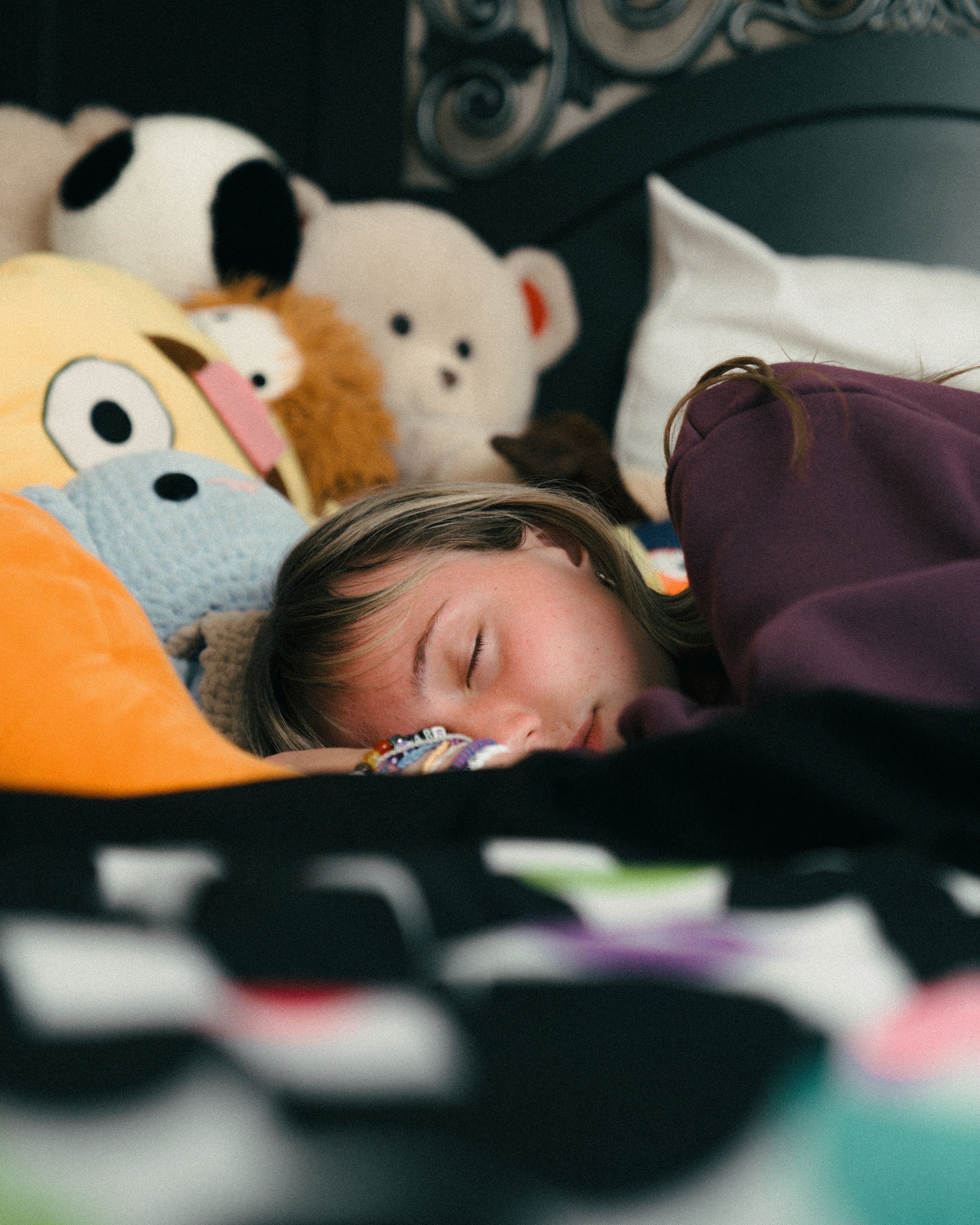 A young girl sleeping on a bed surrounded by stuffed animals, including a panda, lion, and bear.