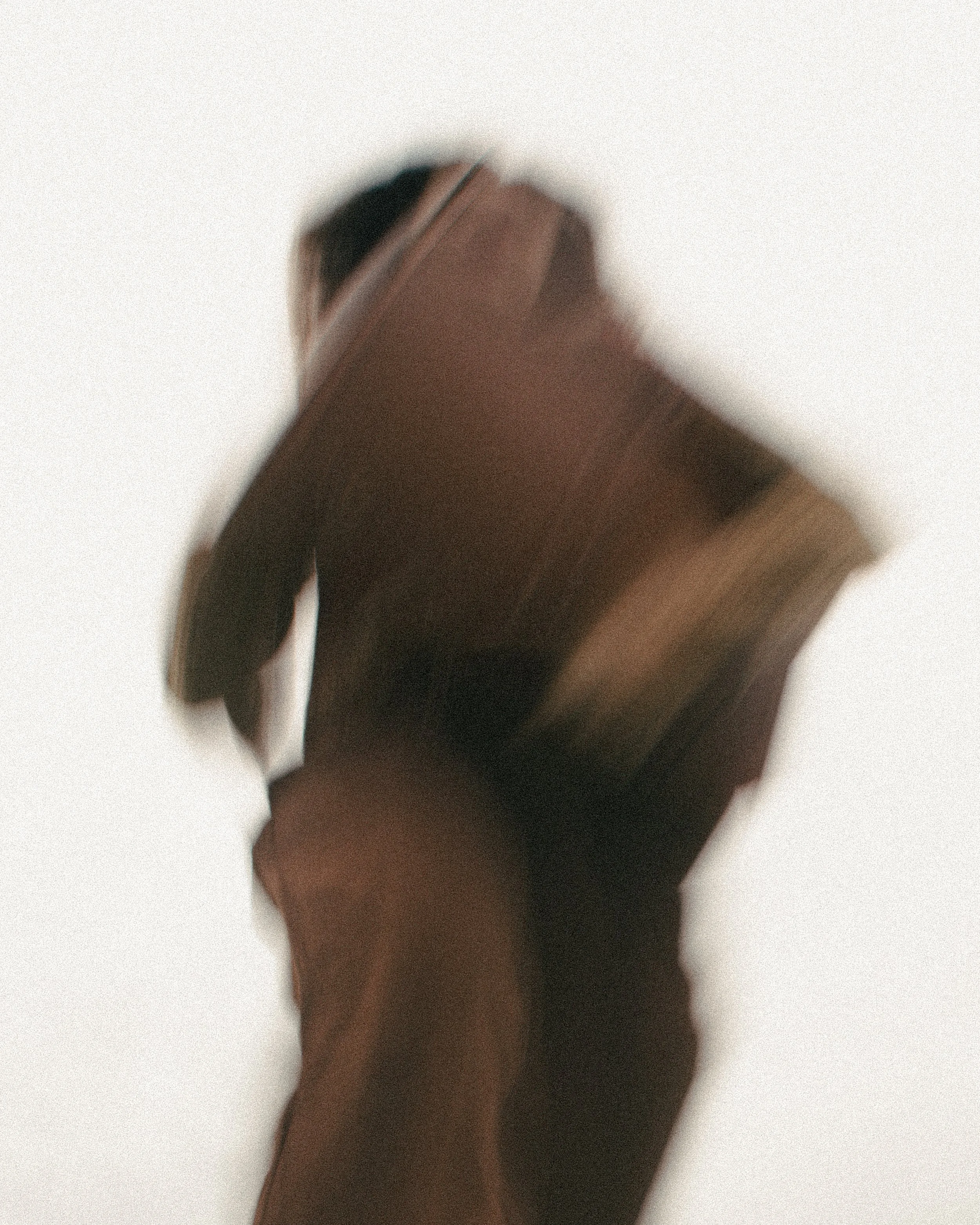 Abstract, blurred image of a person wearing a dark or brown jacket against a light background.