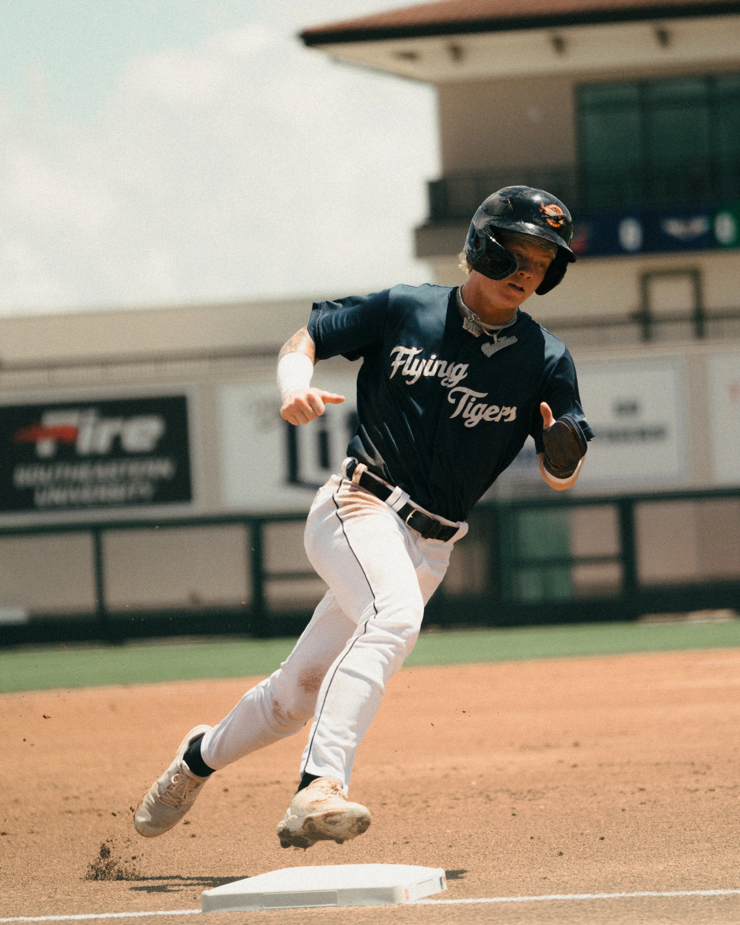 A baseball player running on the base path during a game, wearing a navy blue jersey with 'Flying Tigers' written on it, white pants, and a black helmet.