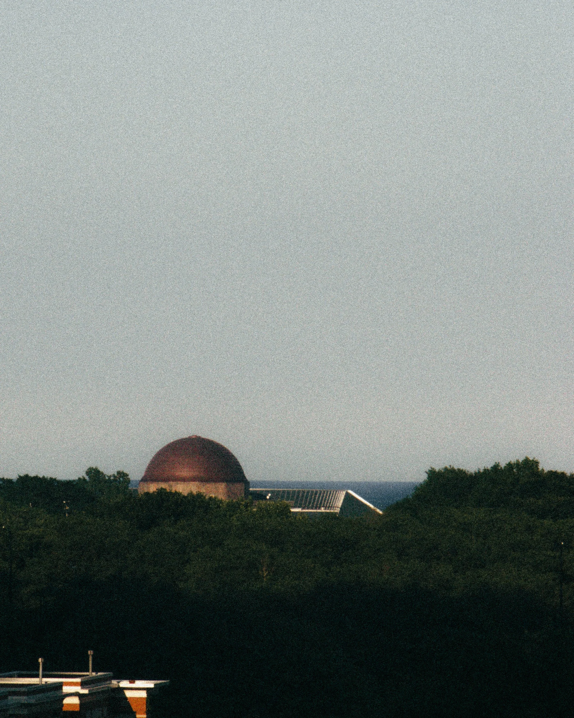 Dome-shaped observatory building with surrounding trees, under a clear sky.