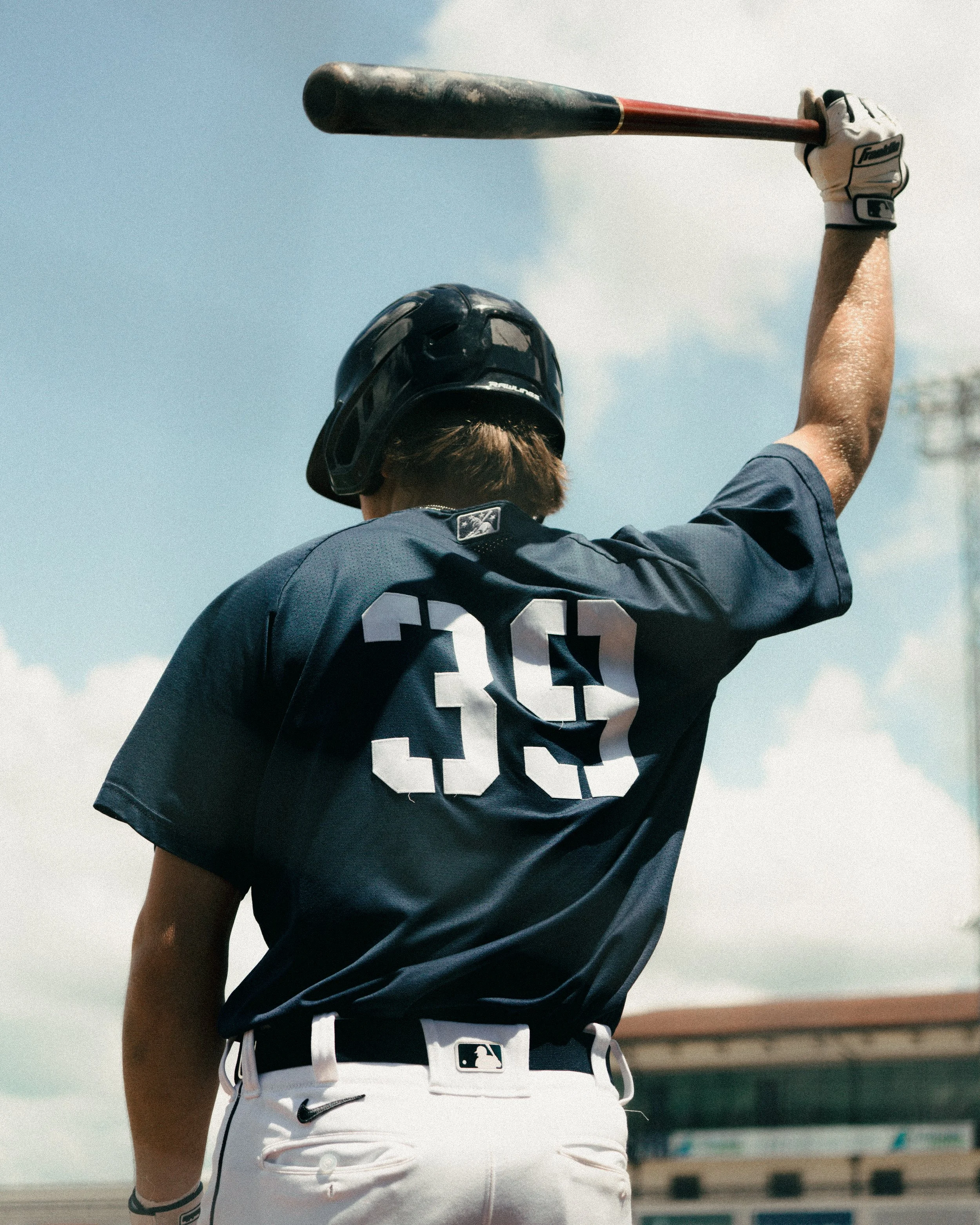 Baseball player with the number 39 on his uniform, raising a bat in the air on a sunny day.