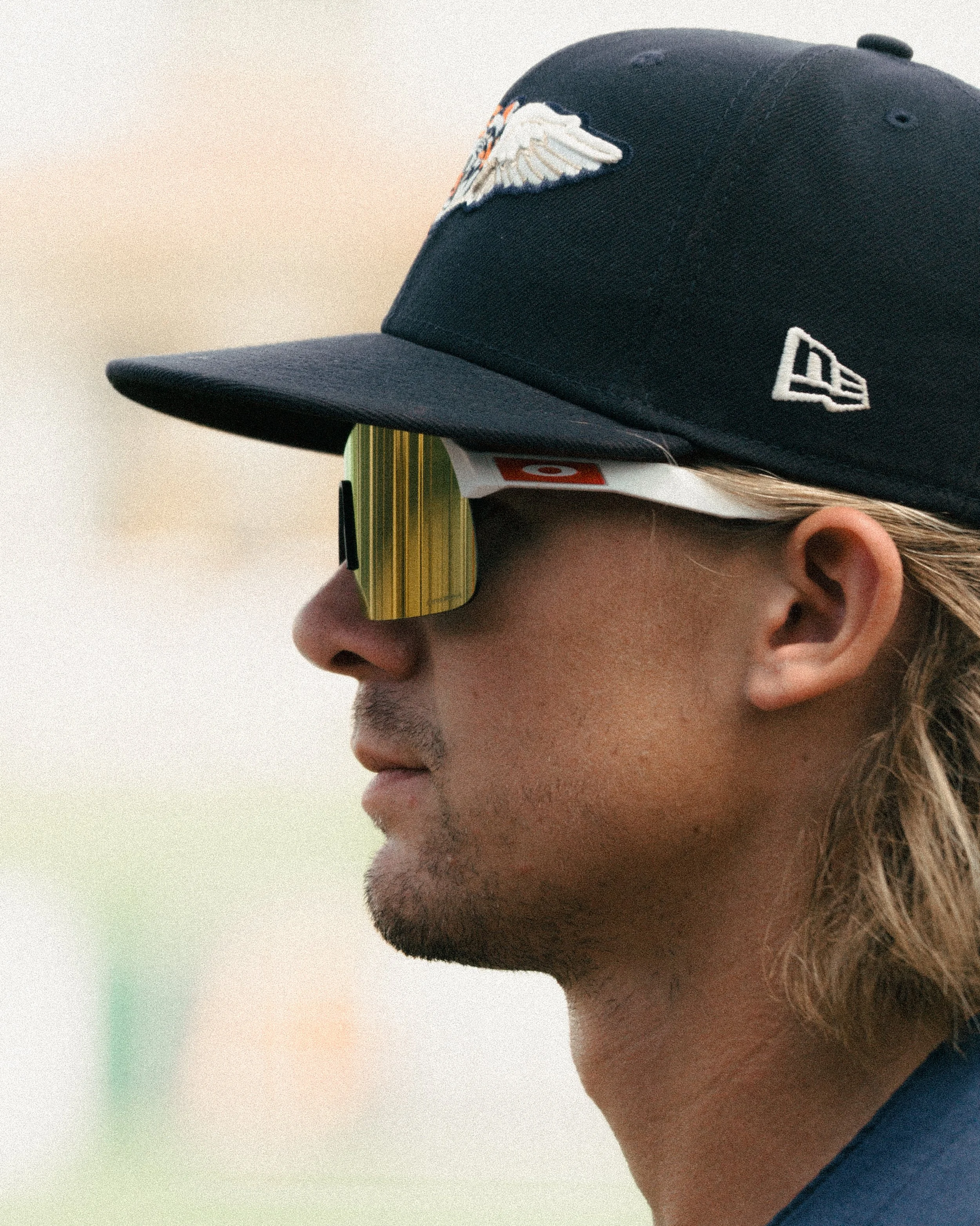 Profile of a man wearing a baseball cap, sunglasses, and a slight beard.