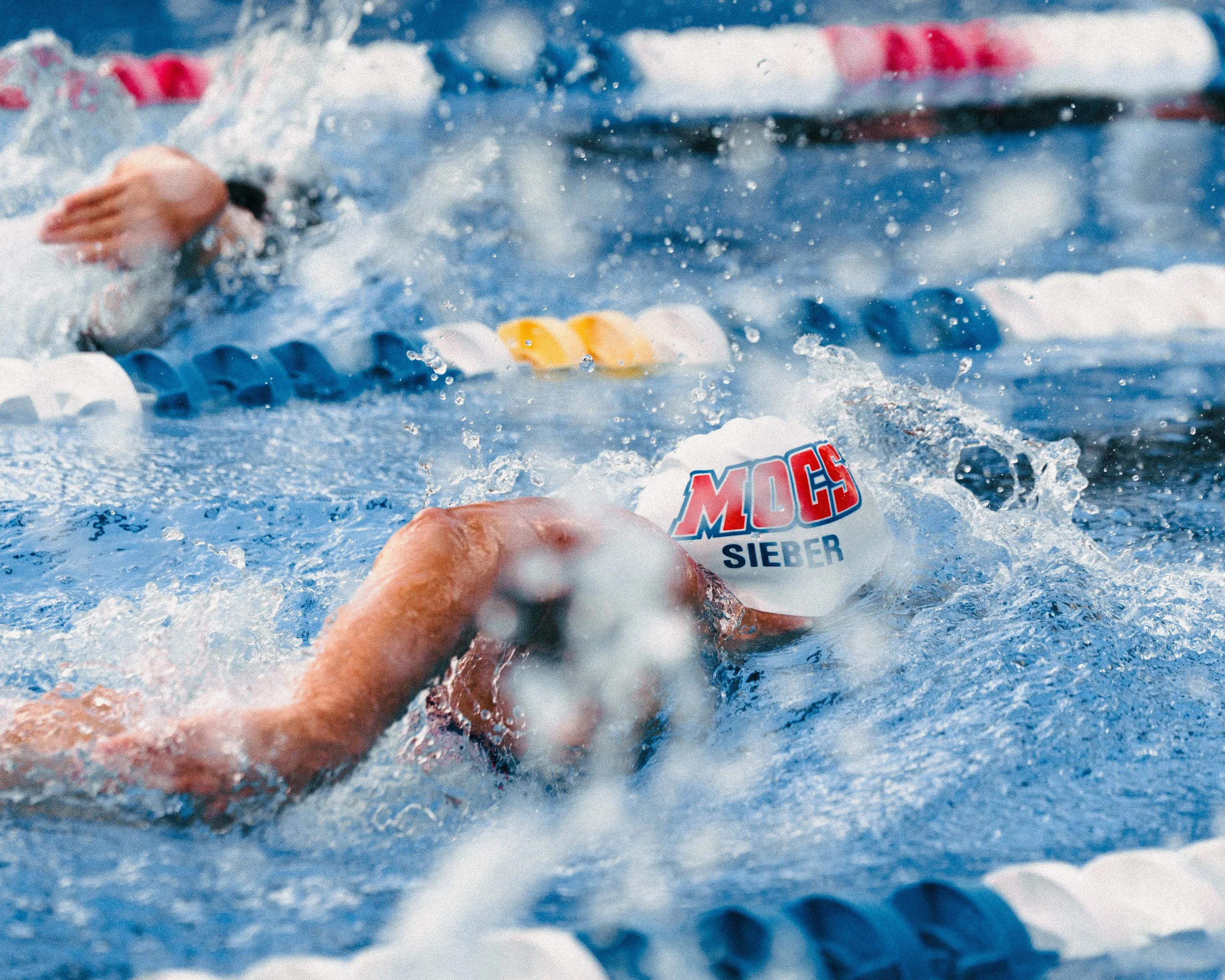 A swimmer in a white cap and goggles participate in a competitive swimming race, swimming freestyle in a pool with lane dividers.