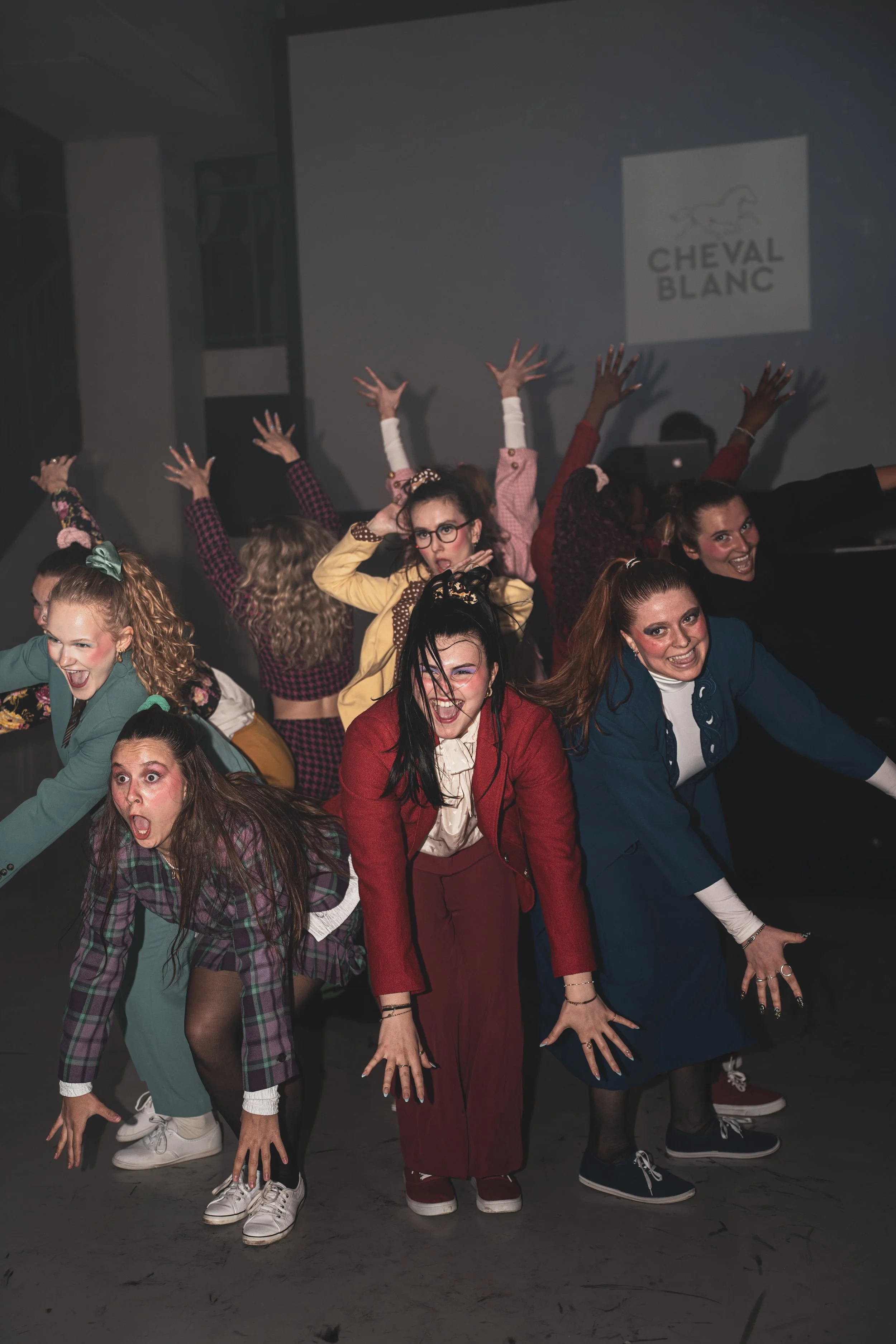 Groupe de femmes déguisées posant en manière expressive lors d'une performance ou d'une fête, avec un logo 'Cheval Blanc' projeté en arrière-plan.