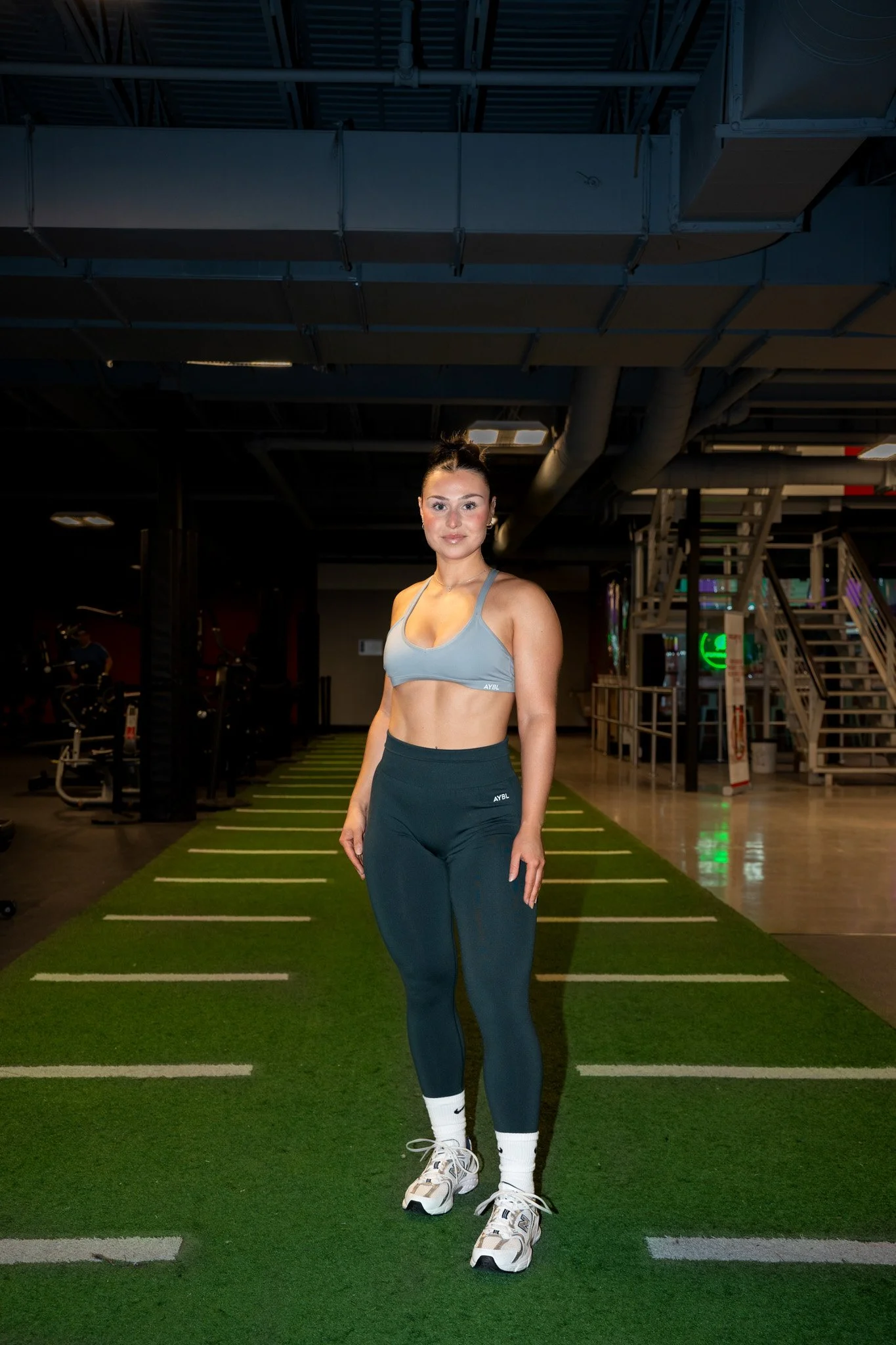 Jeune femme en tenue de sport debout sur un tapis de course dans une salle de sport.