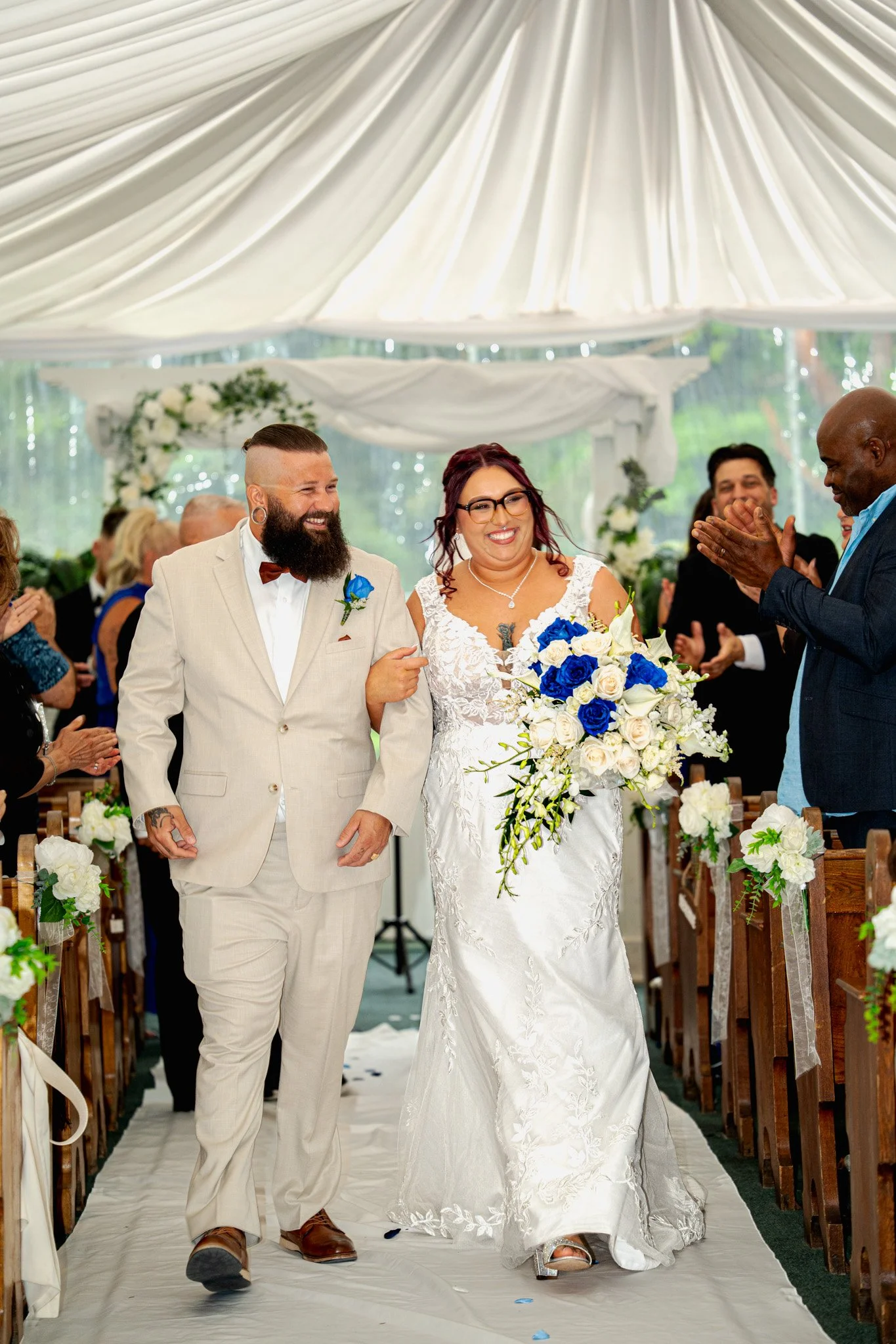Un couple de mariés marchant dans l'allée lors de leur mariage, entouré de invités applaudissant, dans un cadre élégant avec une décoration florale.