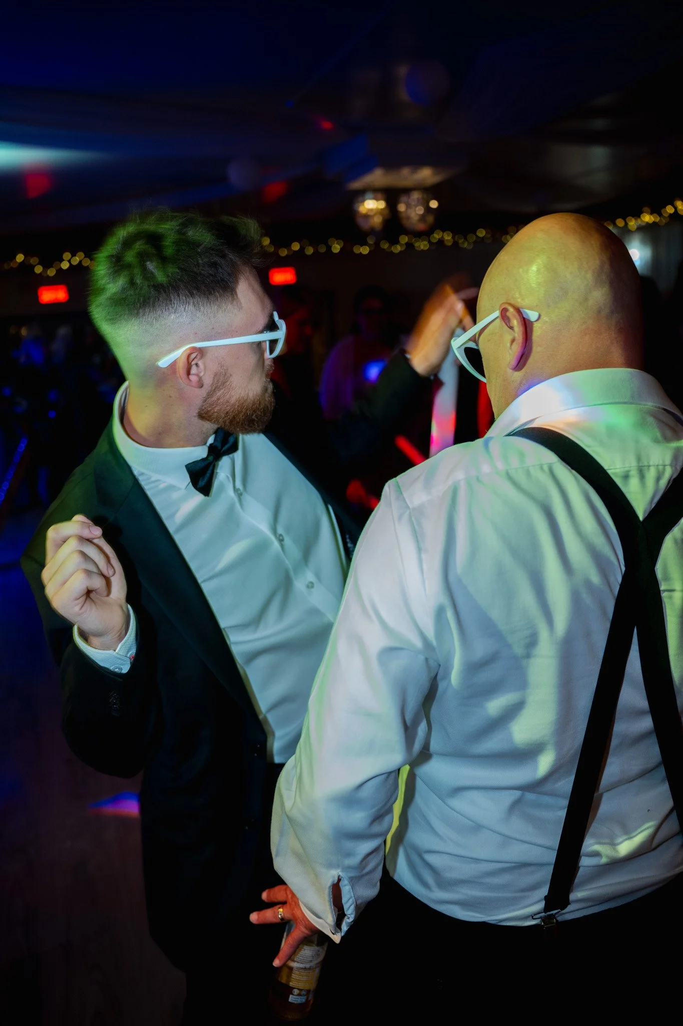 Deux hommes habillés en costume et chemise blanche, portant des lunettes de soleil blanches, dansant lors d'une fête ou d'une soirée dansante