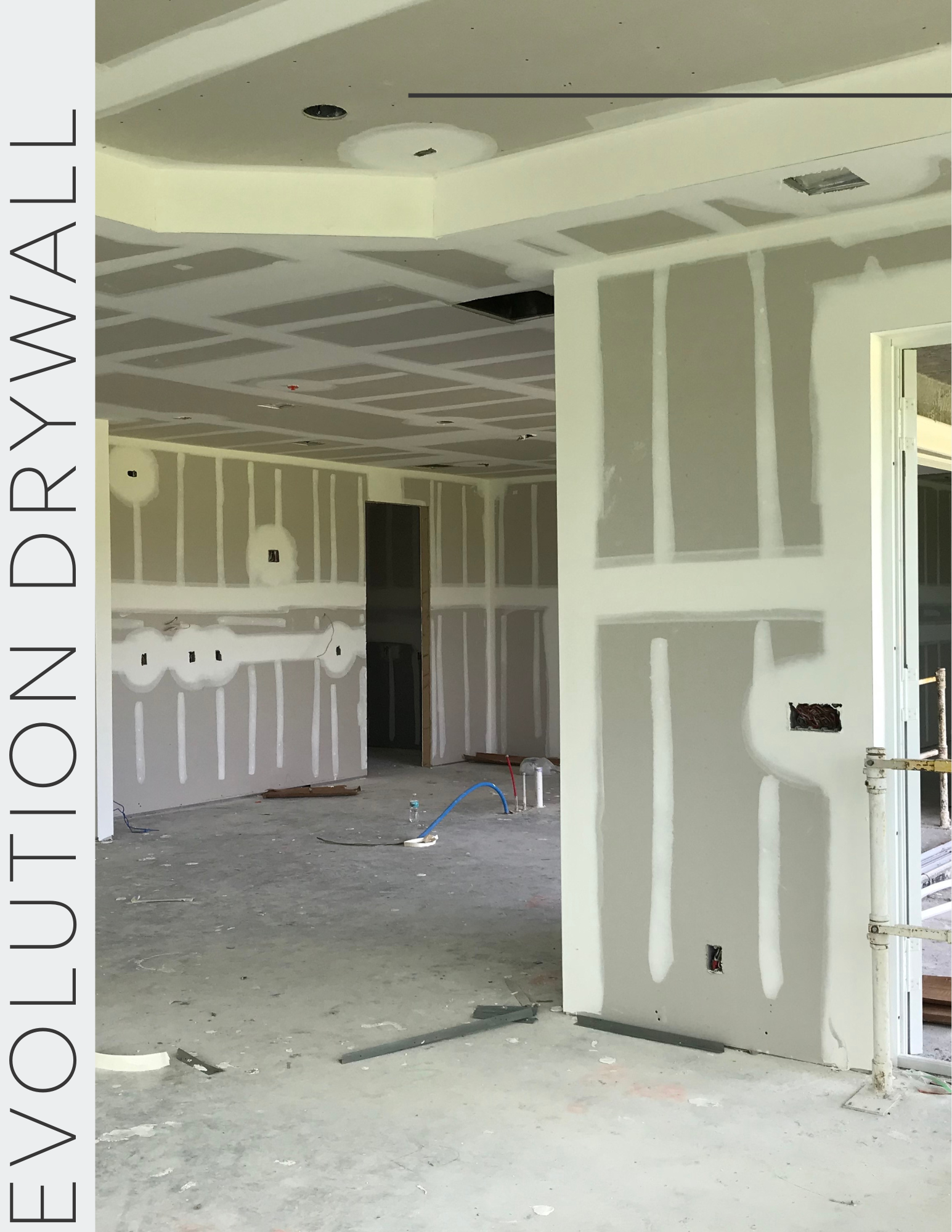 Interior view of a building under construction with unfinished drywall and visible wiring and pipes.