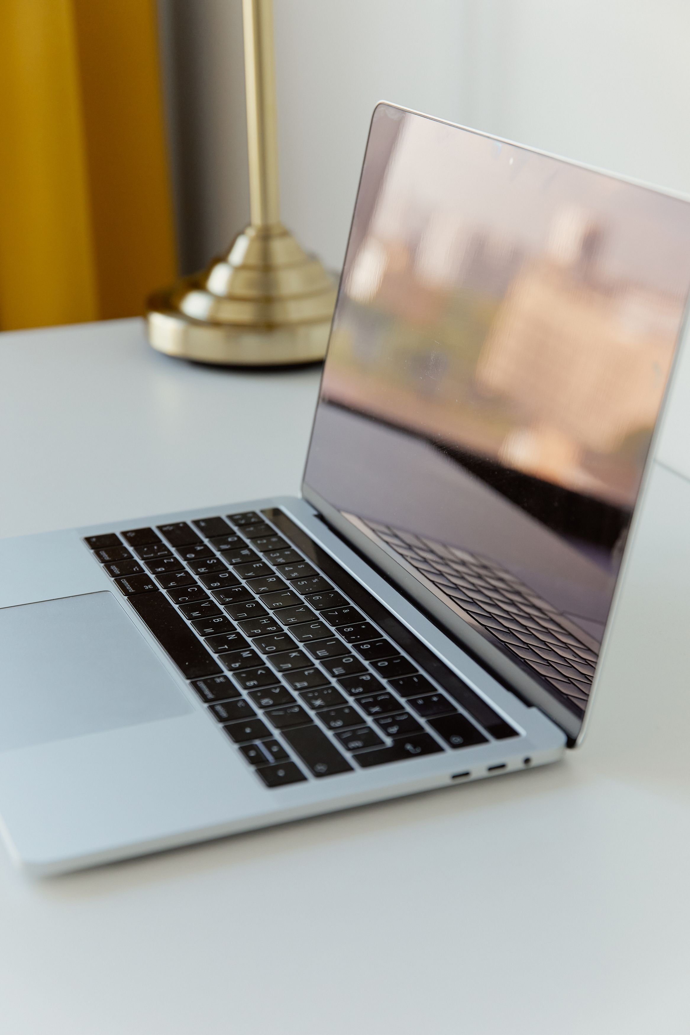 Close-up of an open laptop with a reflective screen on a white surface, a gold desk lamp in the background.