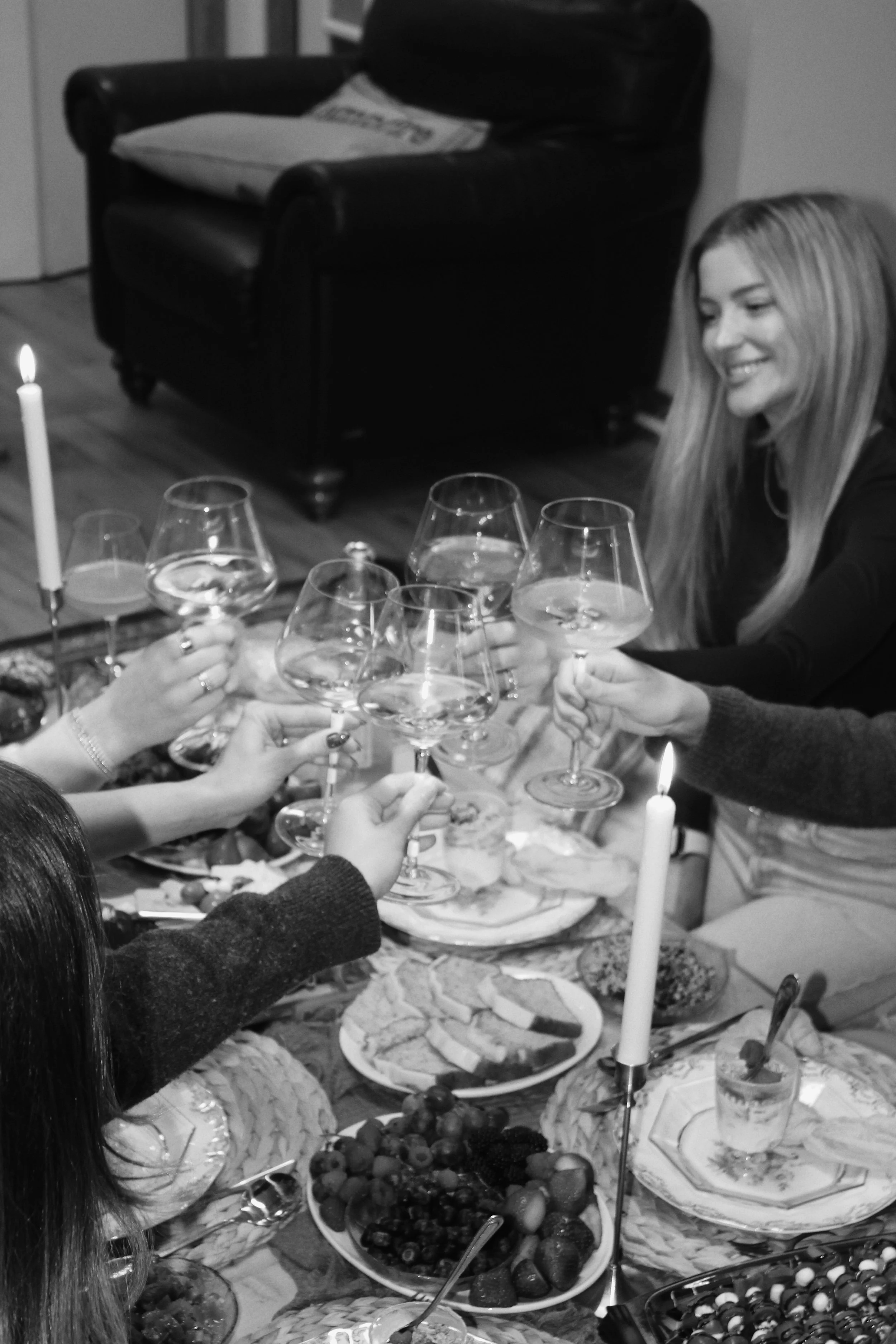 People raising glasses in a toast during a dinner party, with food and candles on the table.