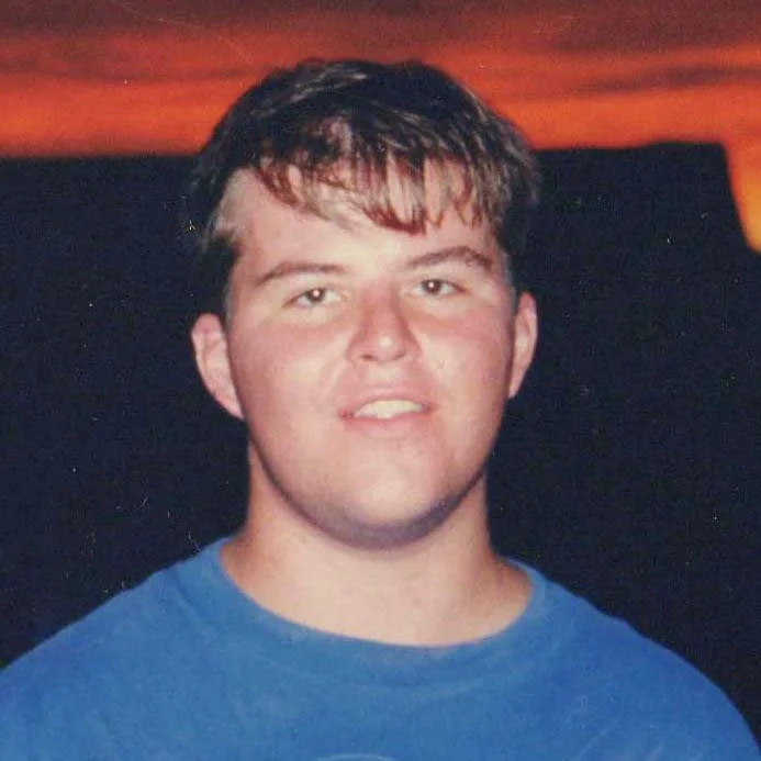 A clean shaven twenty-year-old man with brown hair and a blue shirt.