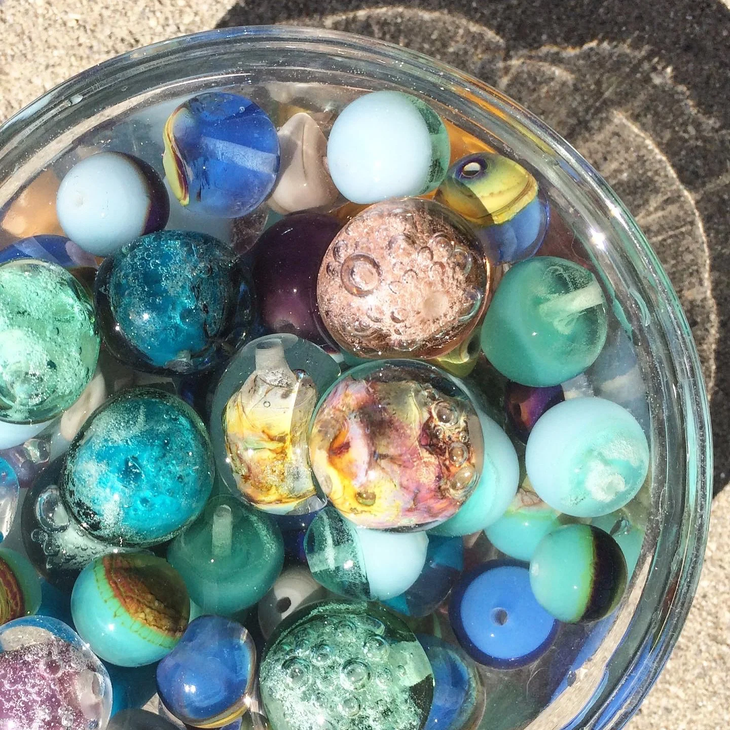 Close-up of a glass bowl filled with various colorful glass beads, some with patterns and bubbles inside.