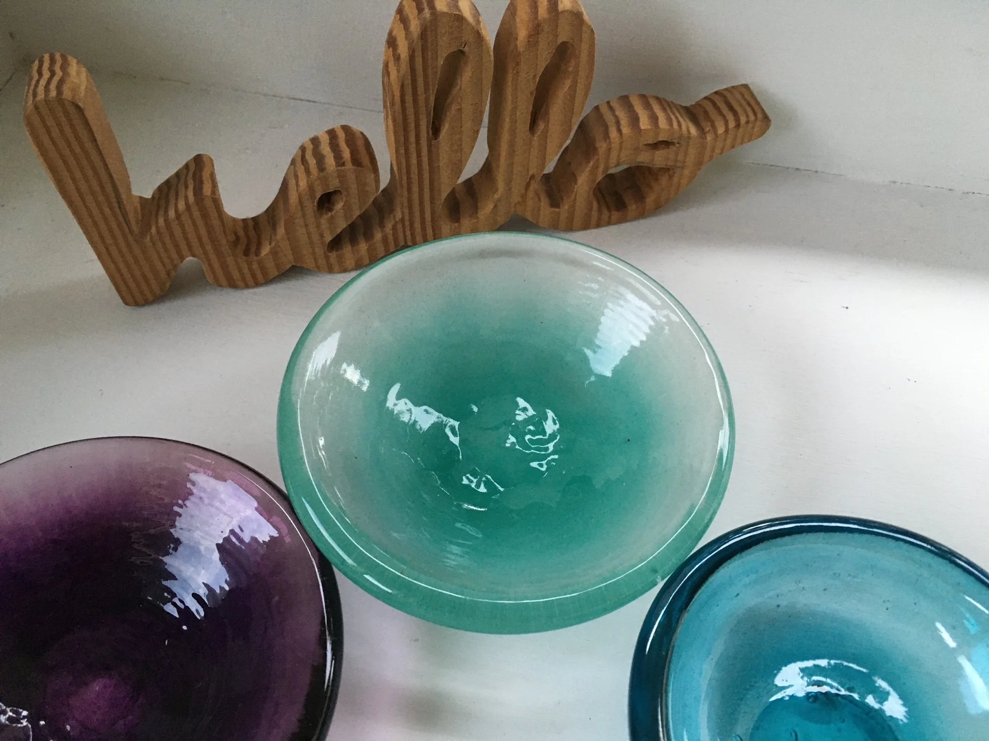 Colorful glass bowls arranged on a white surface, with a wooden decorative piece in the background.