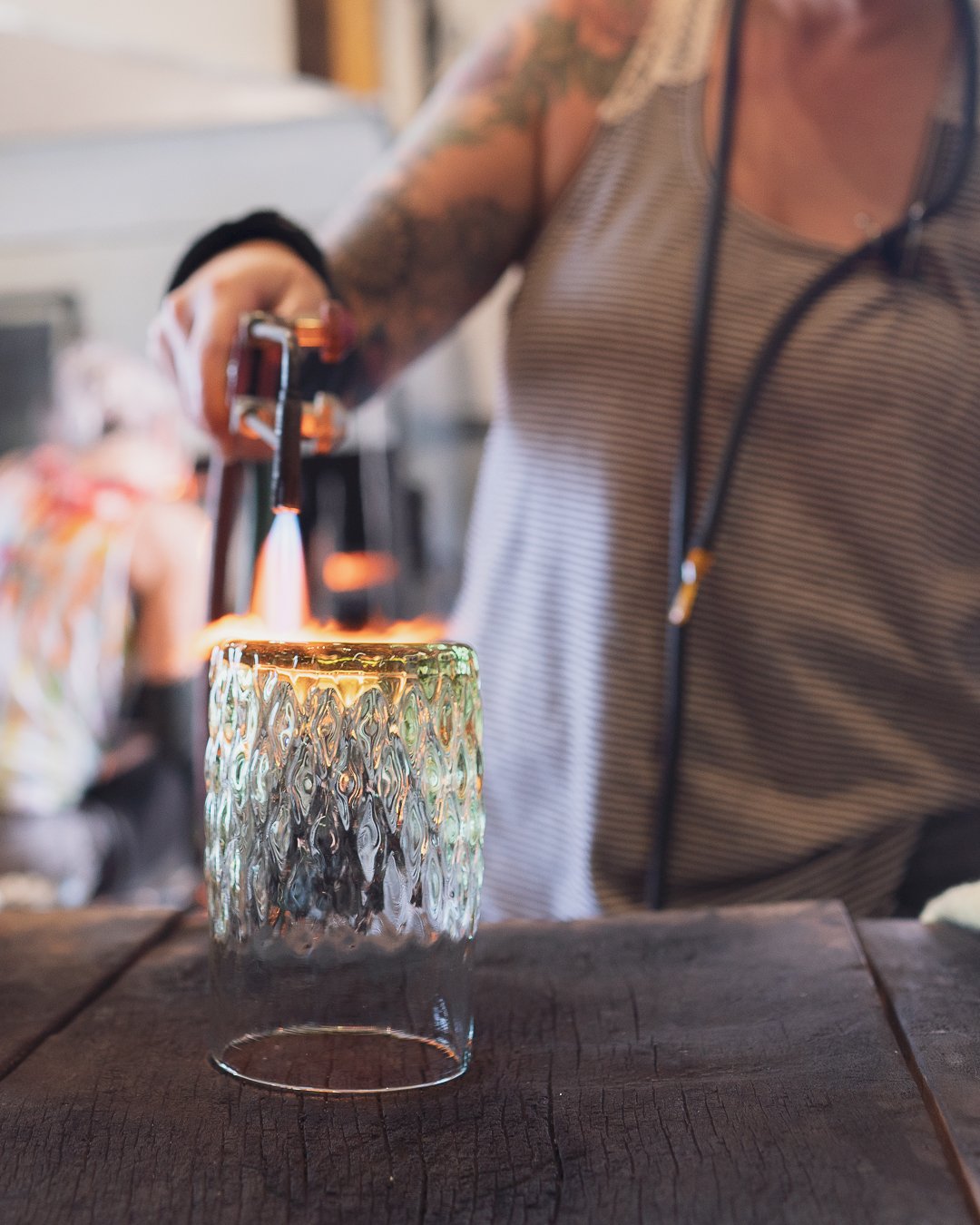 Sonya flame finishing a gem cup glass on a wooden table. The focus is on the glass and the fire action, with a blurred background.