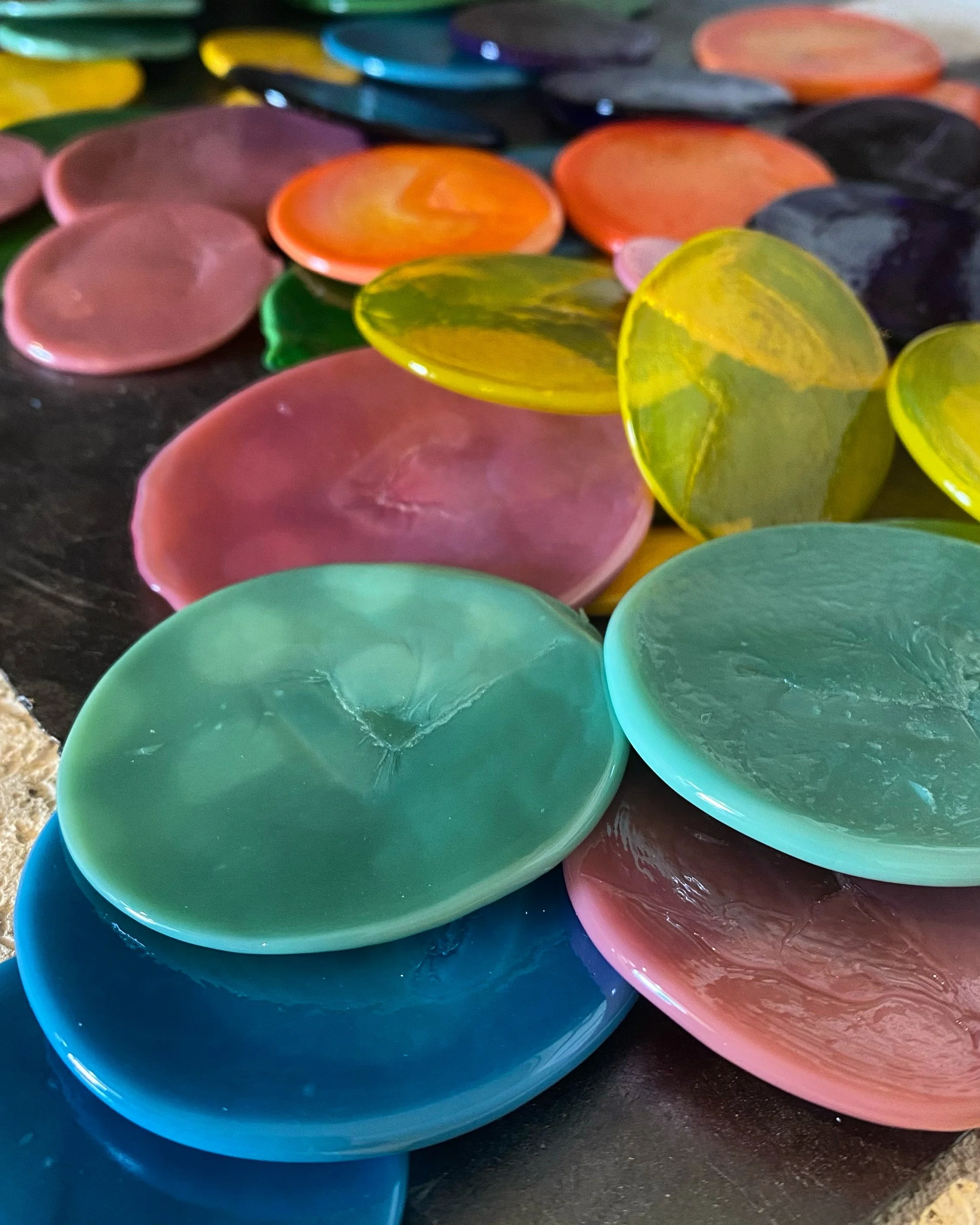 Close-up of a colorful mosaic made of smooth, round, glass stones in shades of pink, orange, yellow, green, blue, and black, arranged on a dark surface.