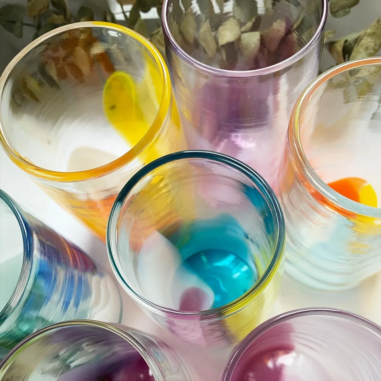 Colorful glass cups viewed from above, each with a different pastel hue, arranged on a white surface.