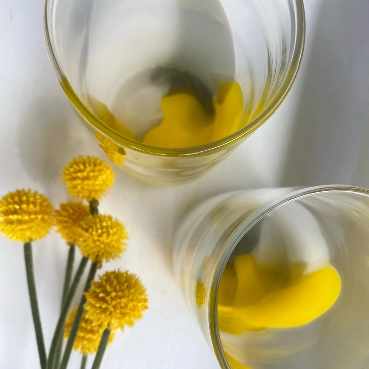 Two  yellow colour pop cups and yellow flower-shaped objects inside, placed on a white surface with yellow flowers nearby.