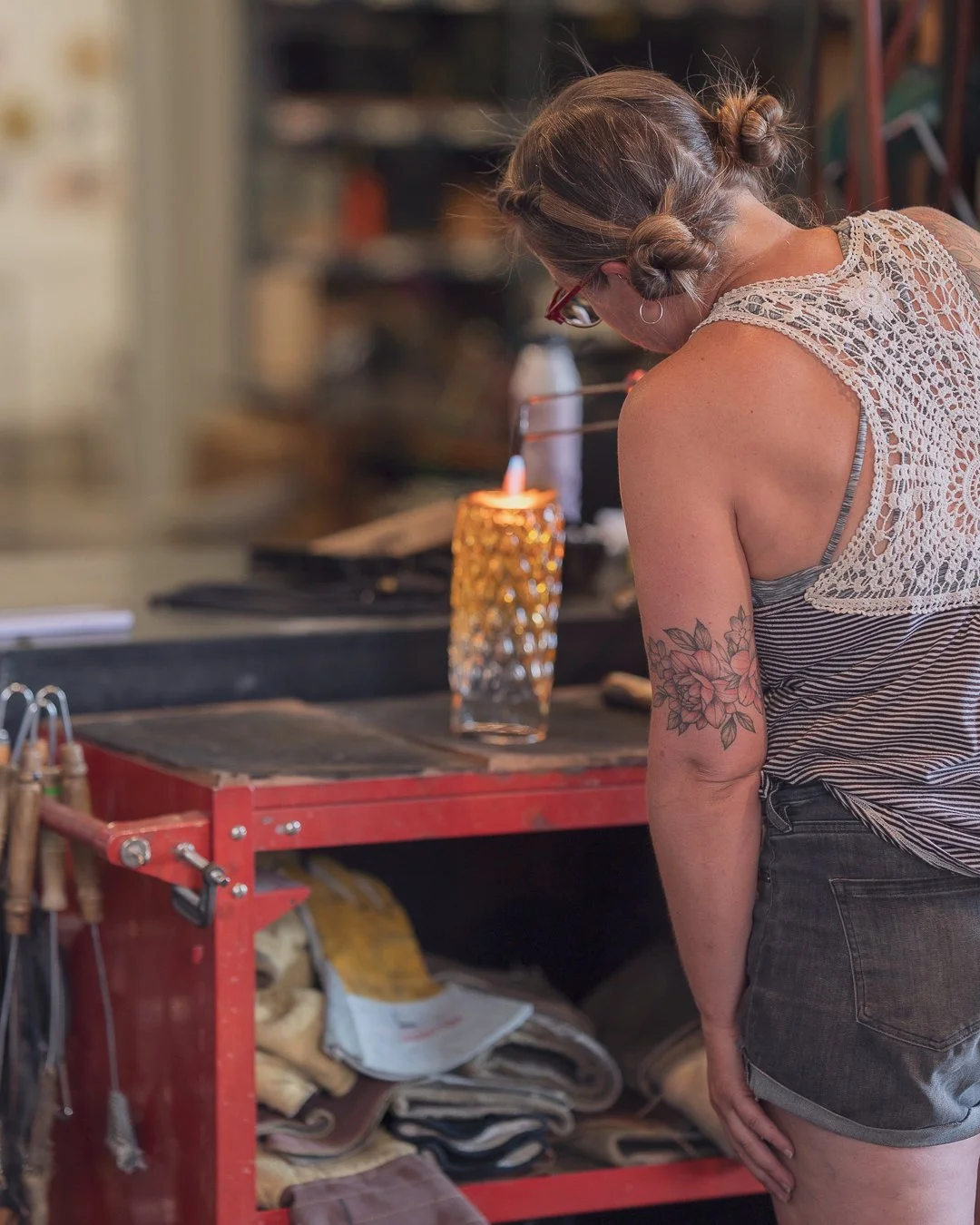 Sonya working in a glassblowing studio, using a long metal rod to shape hot glass over a flame.