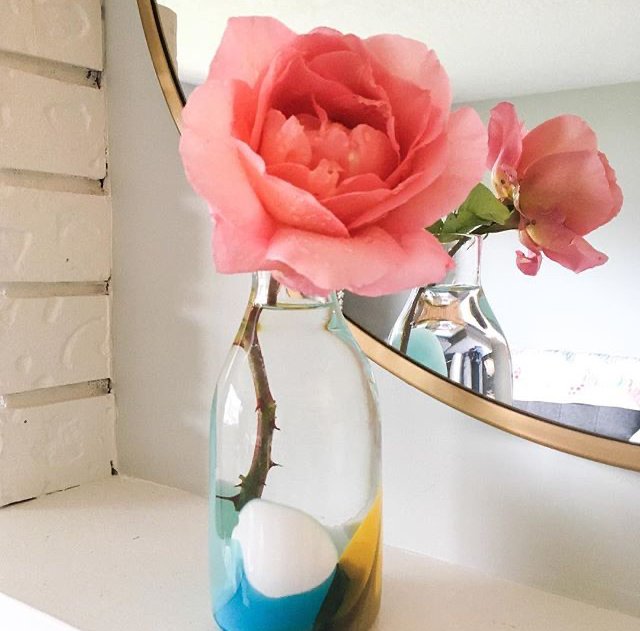 Pink rose in a multicolored colour pop glass vase on a white surface with a mirror in the background.