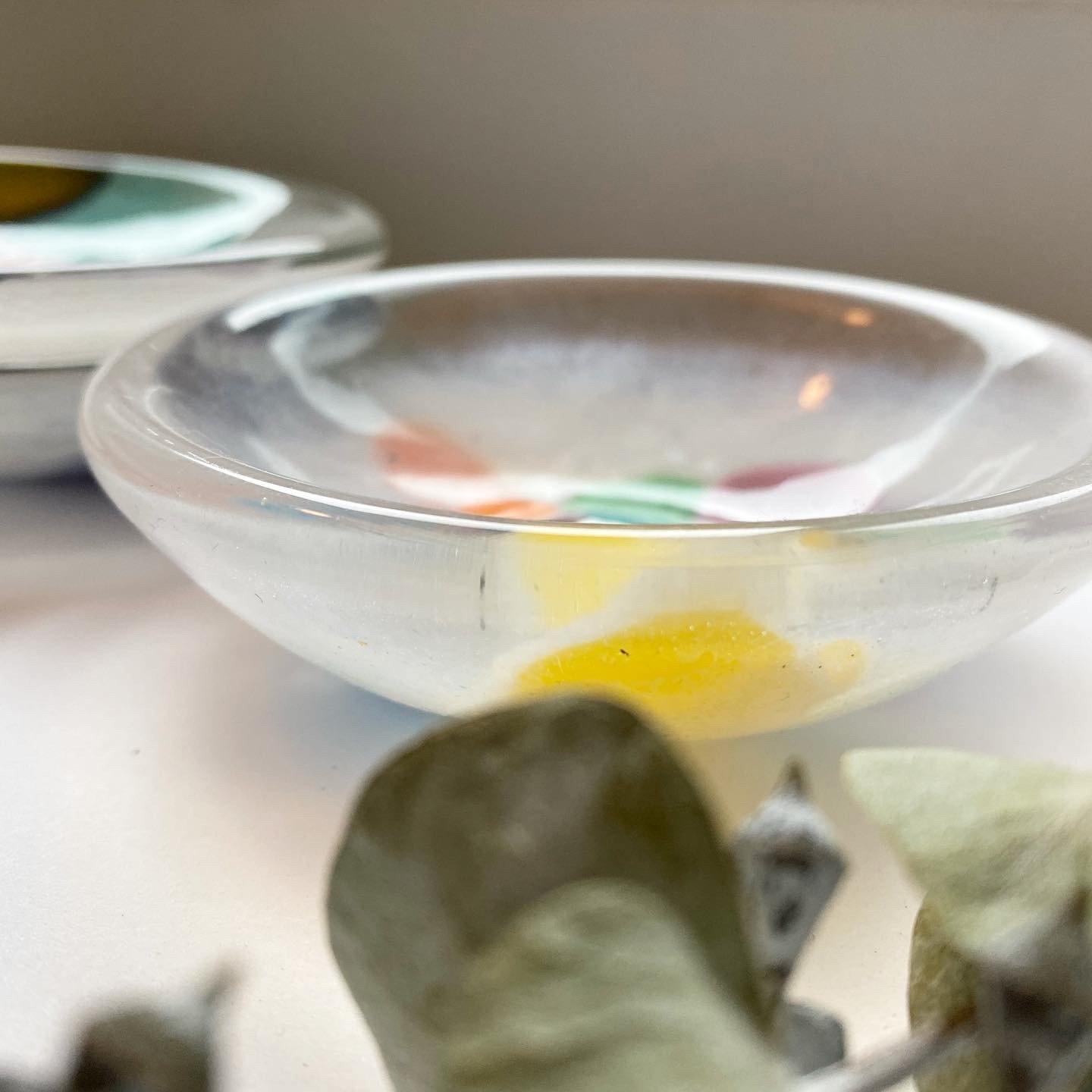 Close-up of glass bowls with colorful patterns and a few dark round objects in the foreground.