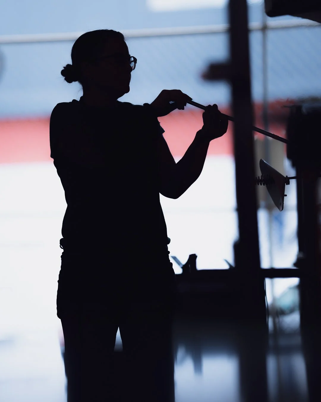 Silhouette of Sonya taking a gather of glass out of the furnace, with bright background light.