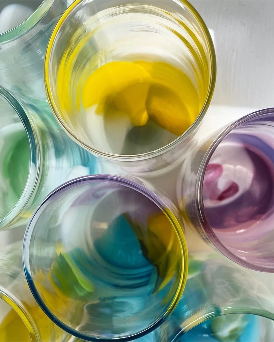 Top-down view of several colorful glass cups, each containing a different colored liquid, arranged closely together.