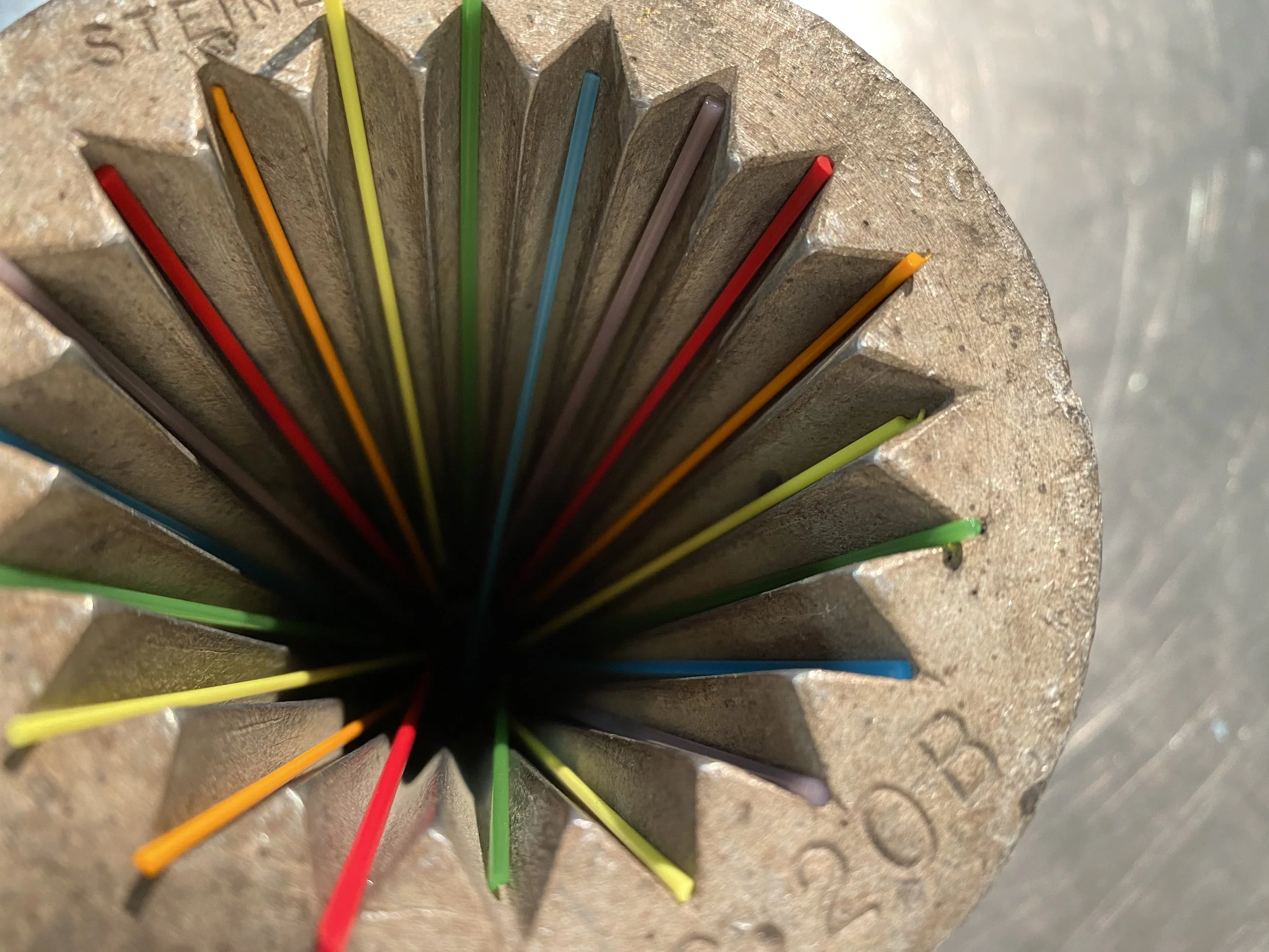 Close-up view inside a blow mold with colorful glass stringers extending from the center, arranged in a radial pattern.