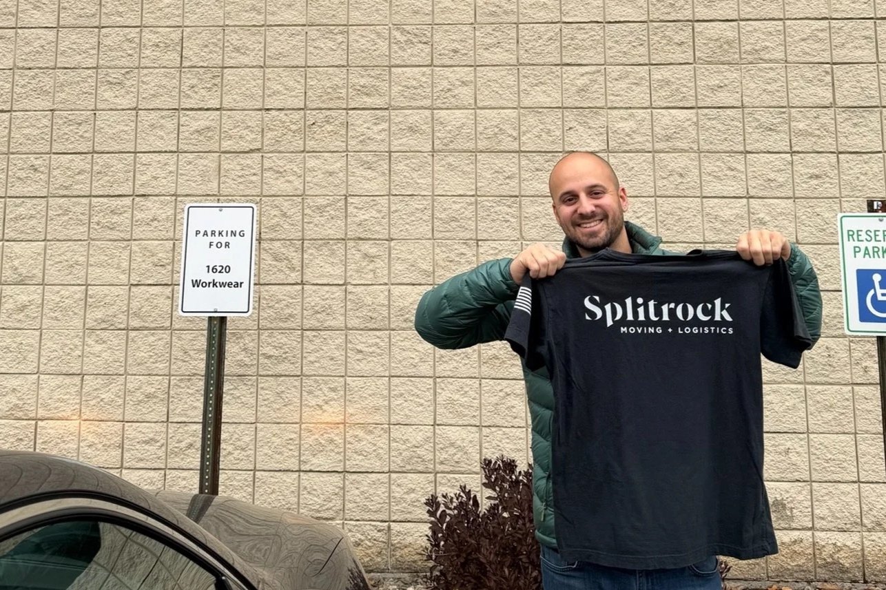 A man smiling and holding a black t-shirt with 'Splitrock Moving + Logistics' printed on it.