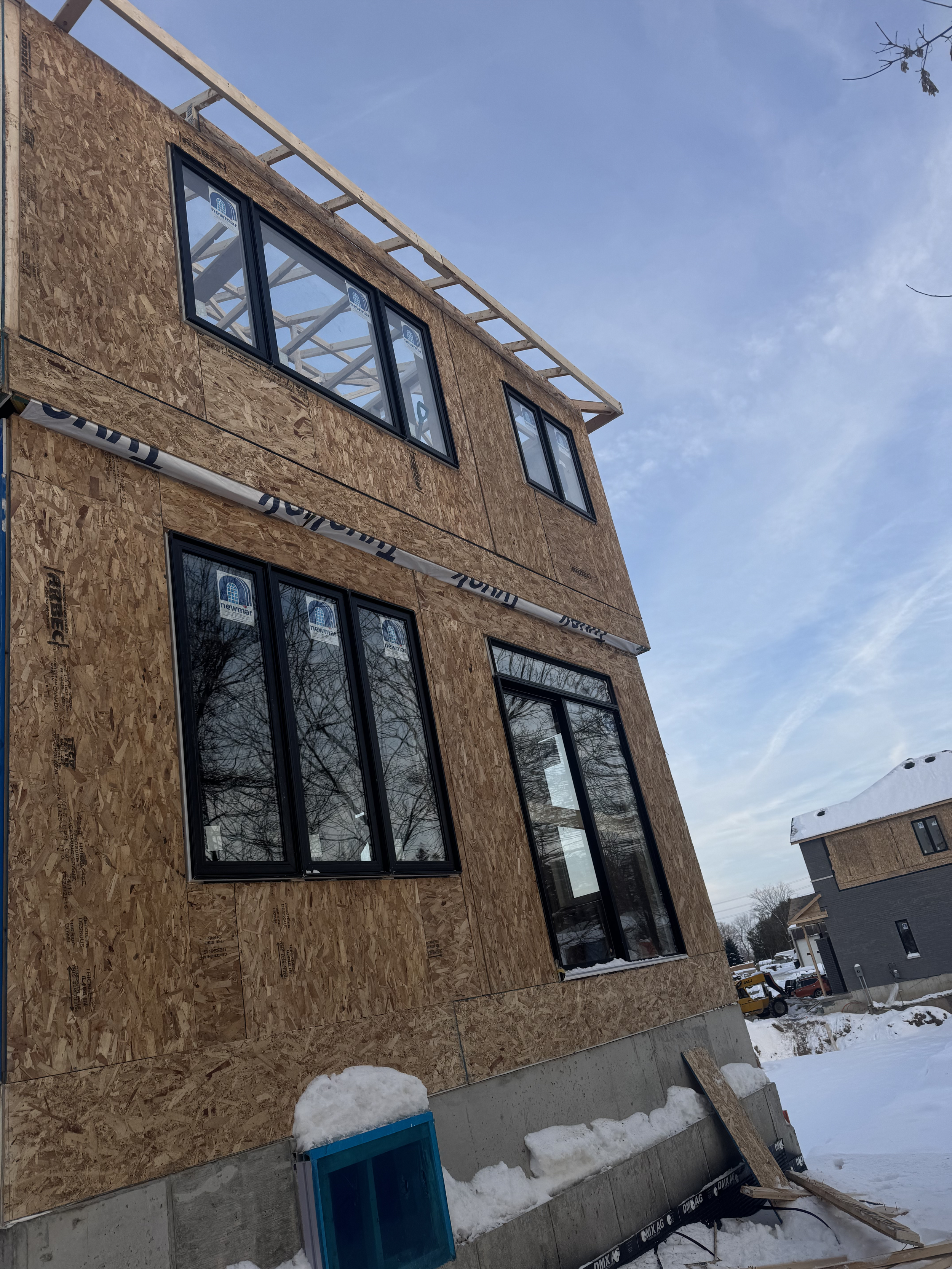 Construction of a multi-story building with wooden sheathing, black-framed windows, and snow on the ground. The building is in an early stage of construction.