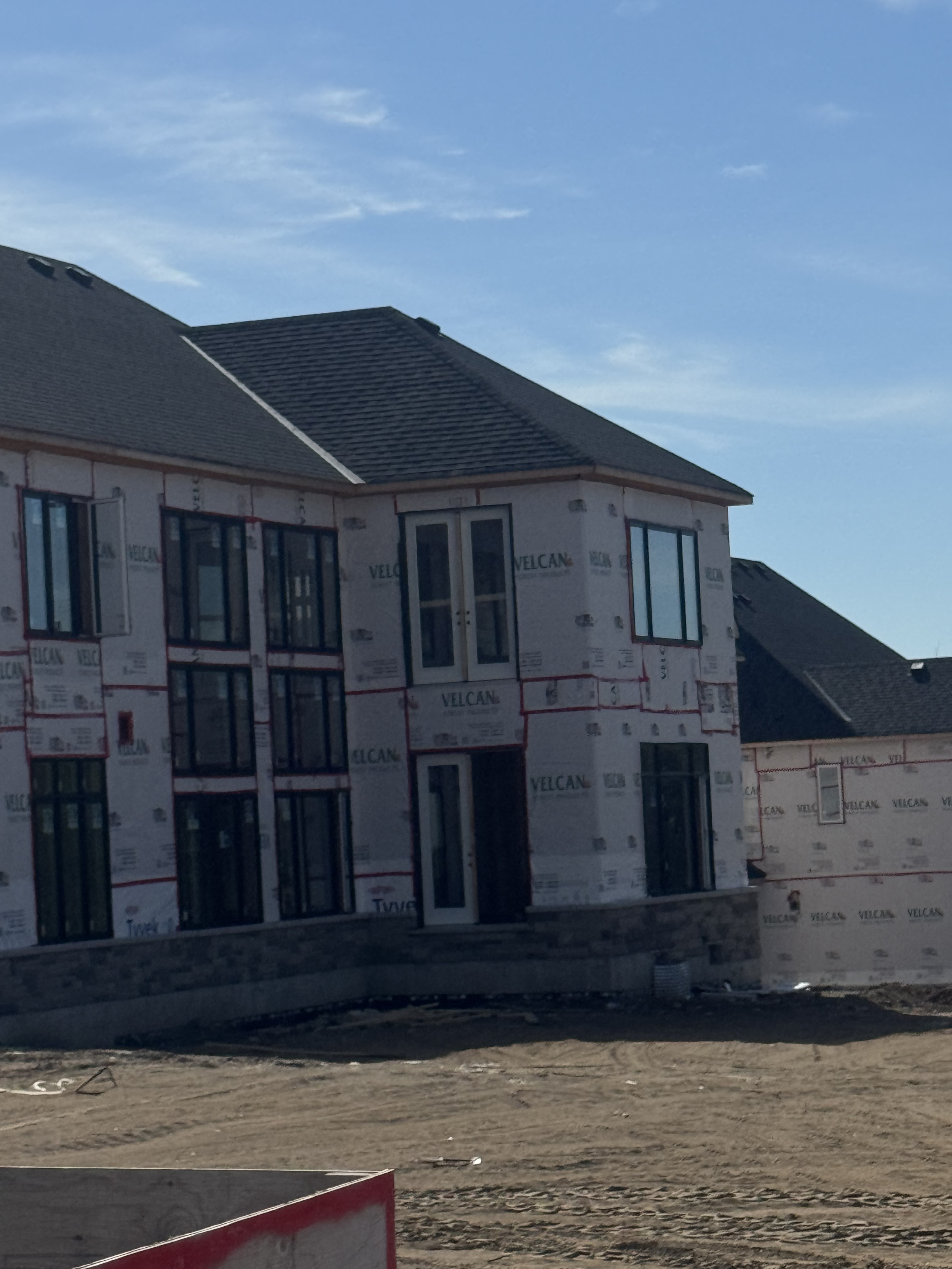 Under-construction house with multiple windows, surrounded by dirt, under a blue sky.