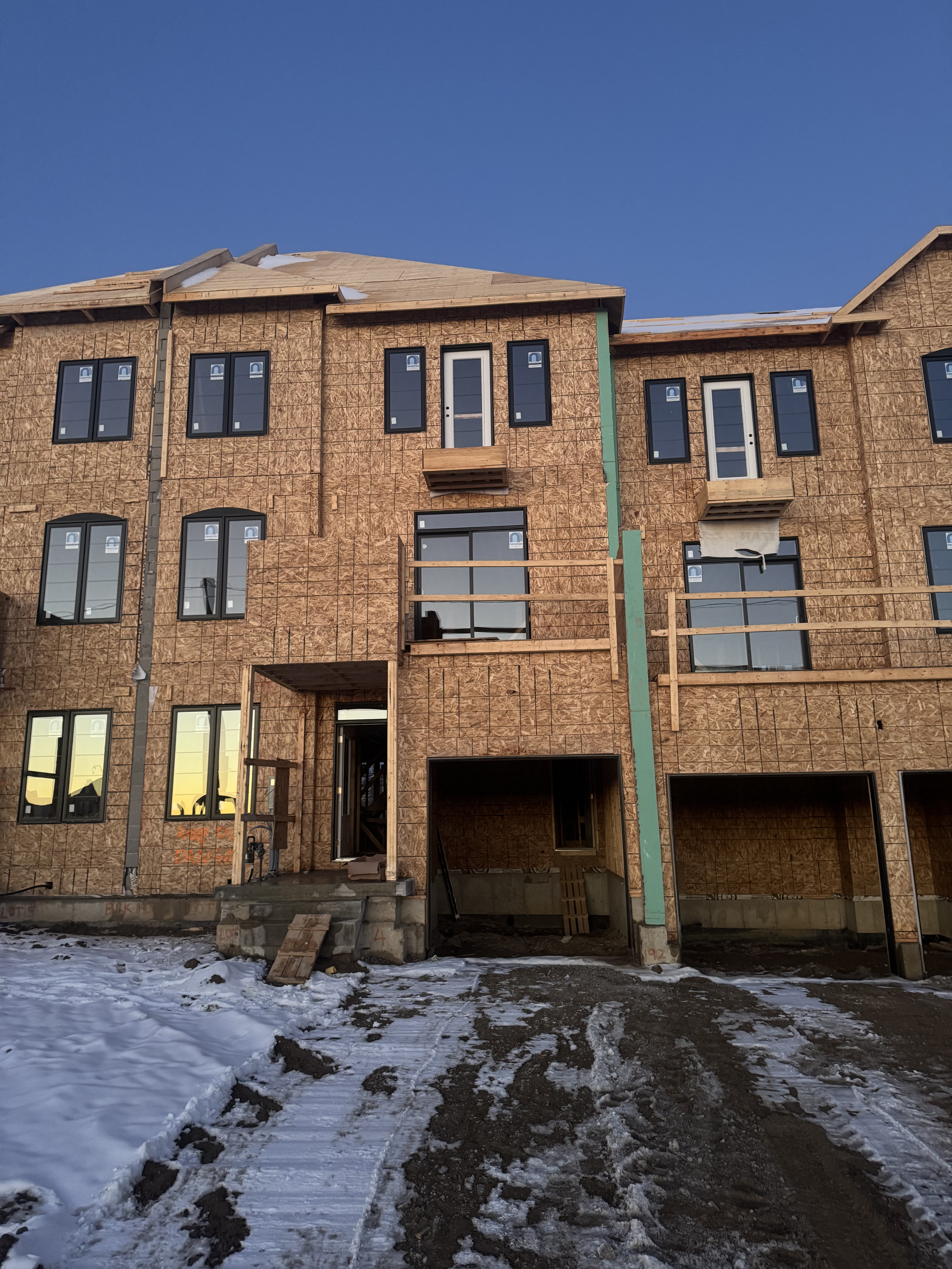 Under-construction multi-story building with exposed wooden framing, scaffolding, and snow on the ground, during sunset.