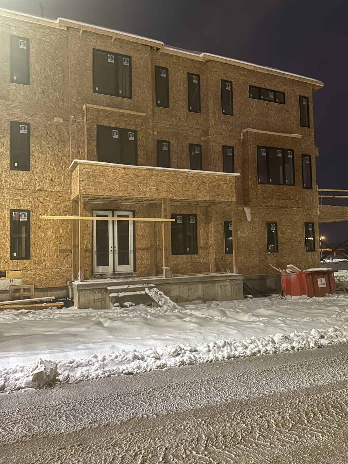 A wooden house under construction at night, with snow on the ground and a dark sky in the background.