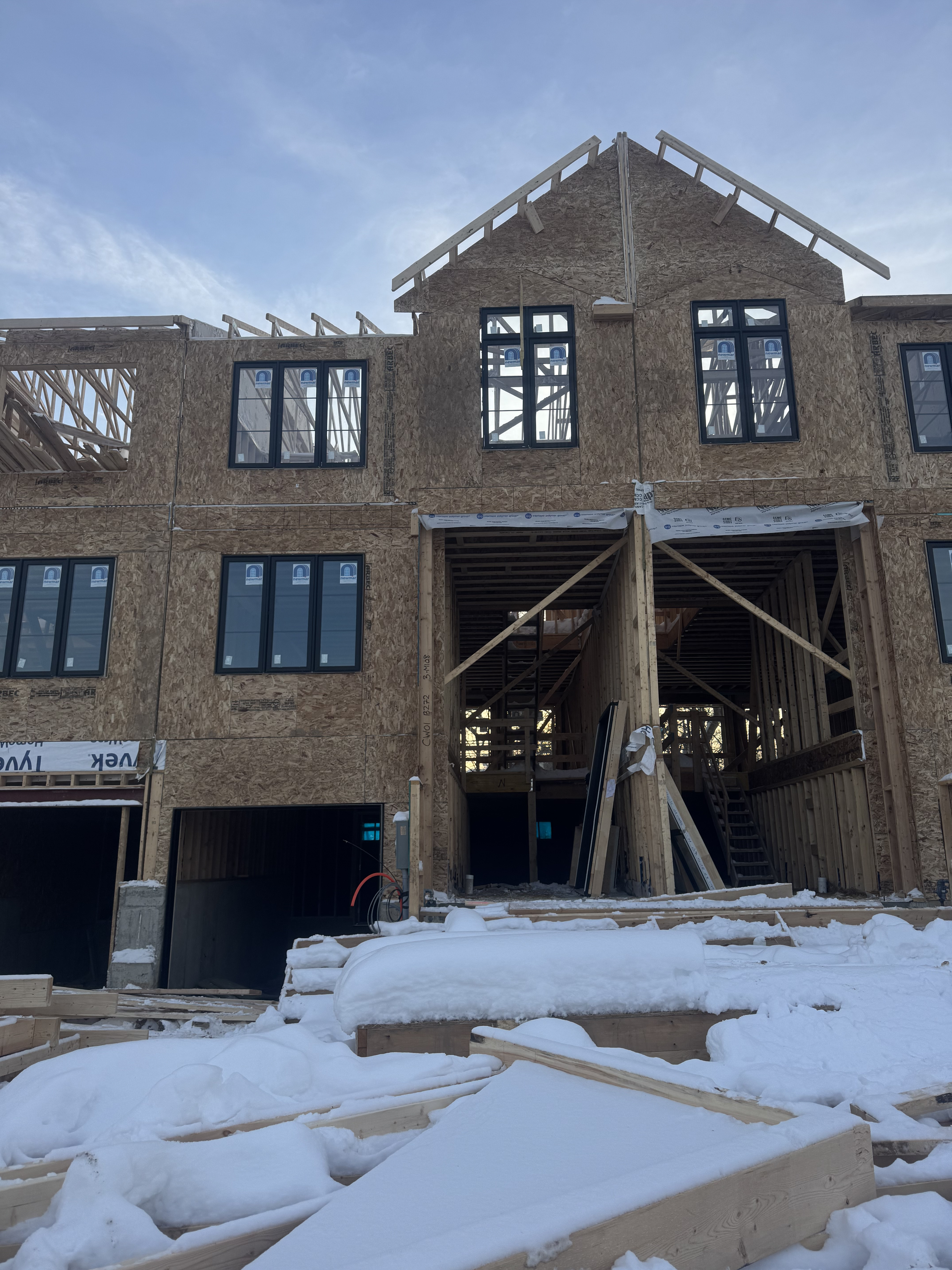 Under construction multi-story residential building with exposed wooden framing, snow-covered ground, and partially installed windows.