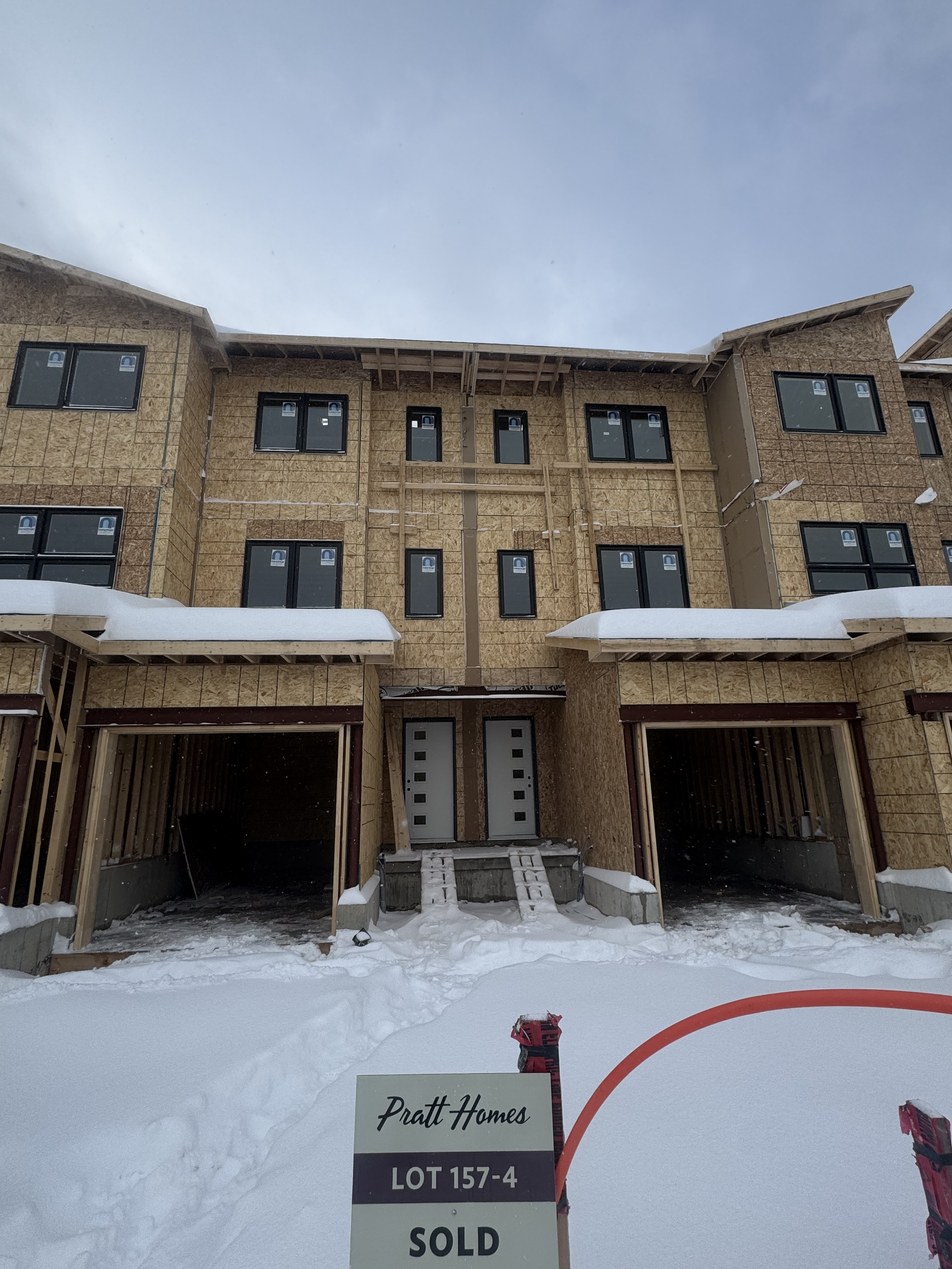 Under construction multi-story house with windows and snow on the ground, sign indicating lot 157-4 is sold.