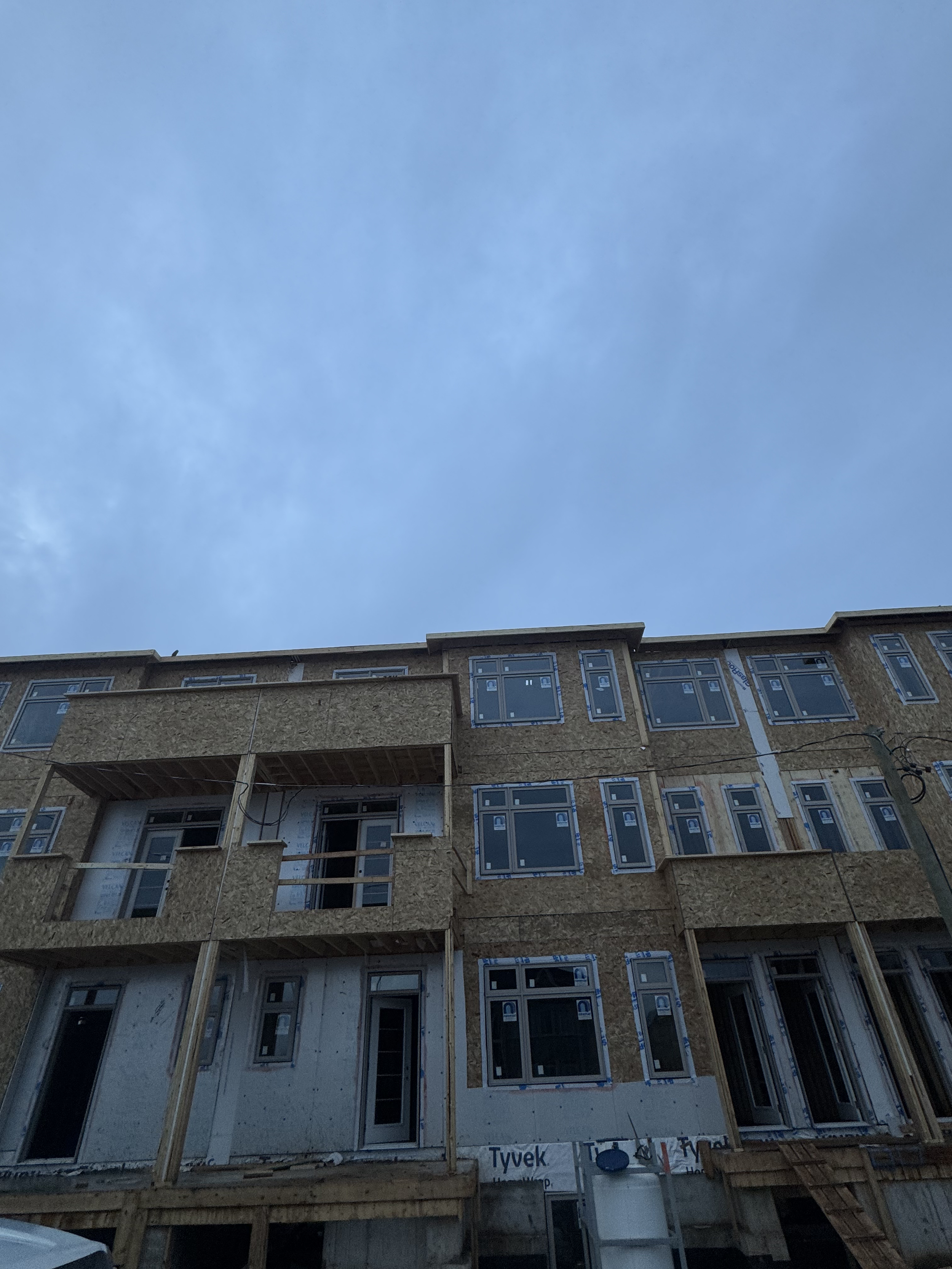Under construction multi-story residential building with exposed framing, windows, and doors, with a darkening sky above.