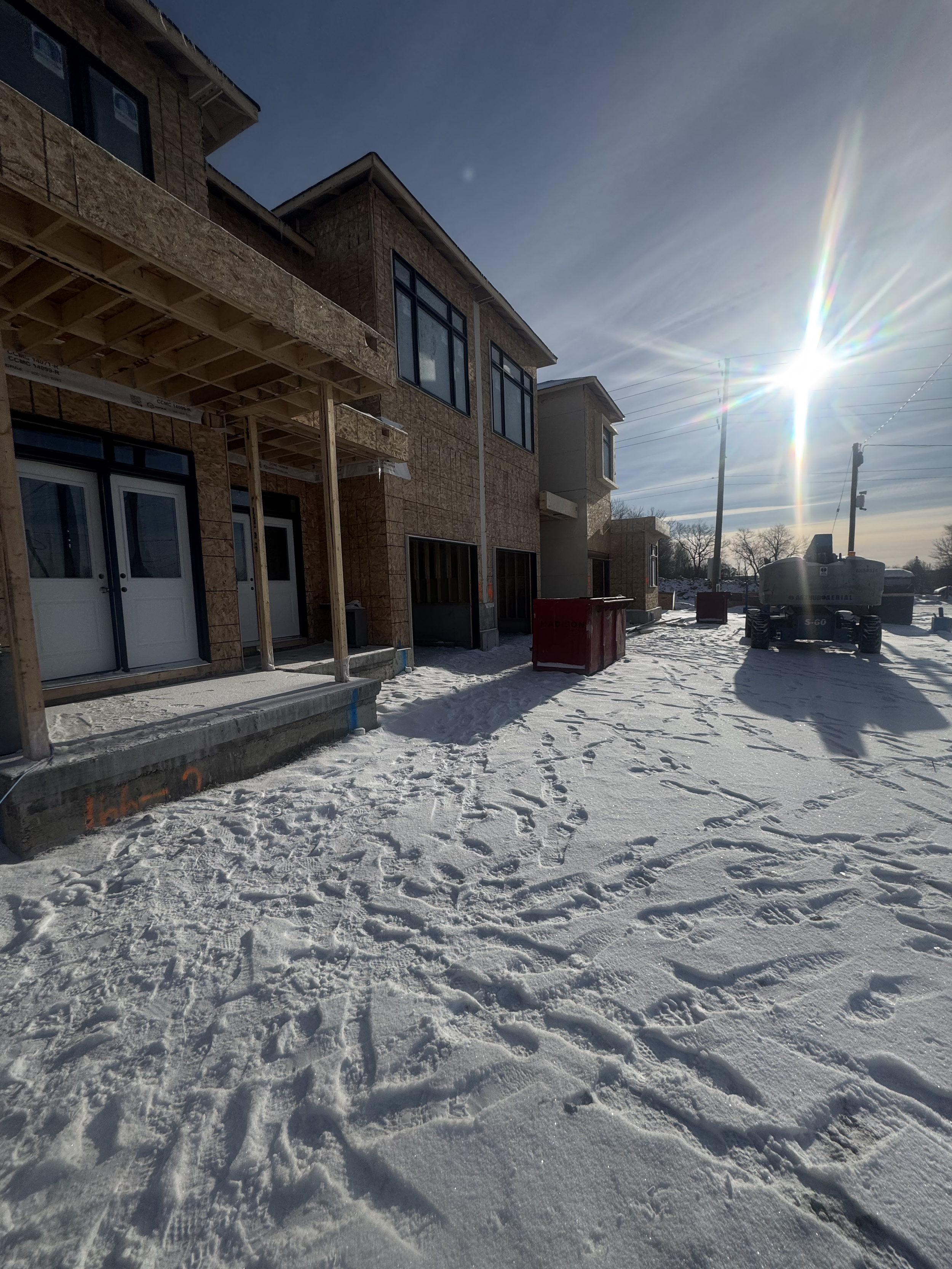 Construction site of a multi-story building with wooden framing, surrounded by snow, with construction equipment and tools visible, under a blue sky with sunlight.