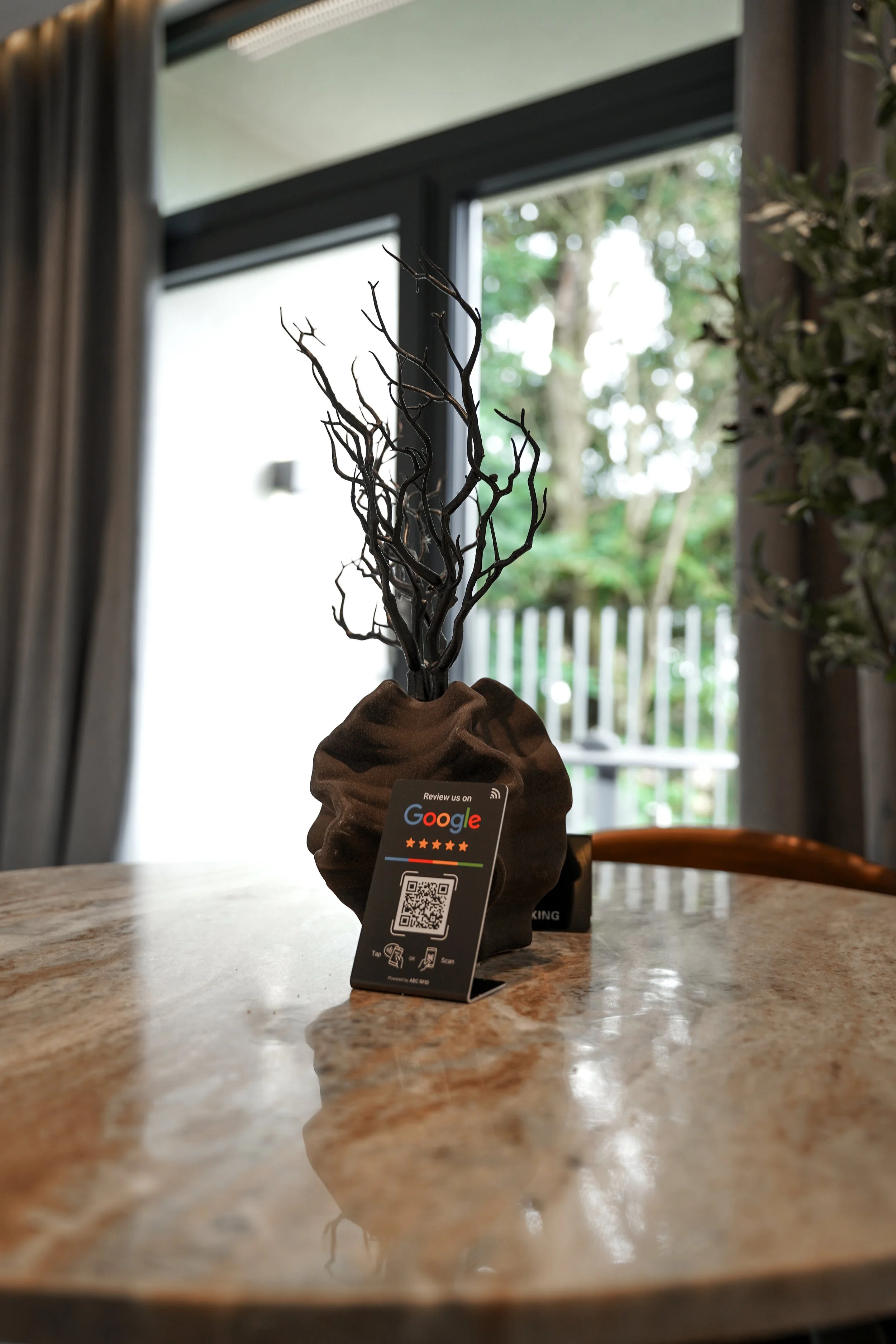 Deko-Blume auf einem Tisch mit QR-Code-Stand, im Hintergrund große Fenster mit Blick nach draußen.