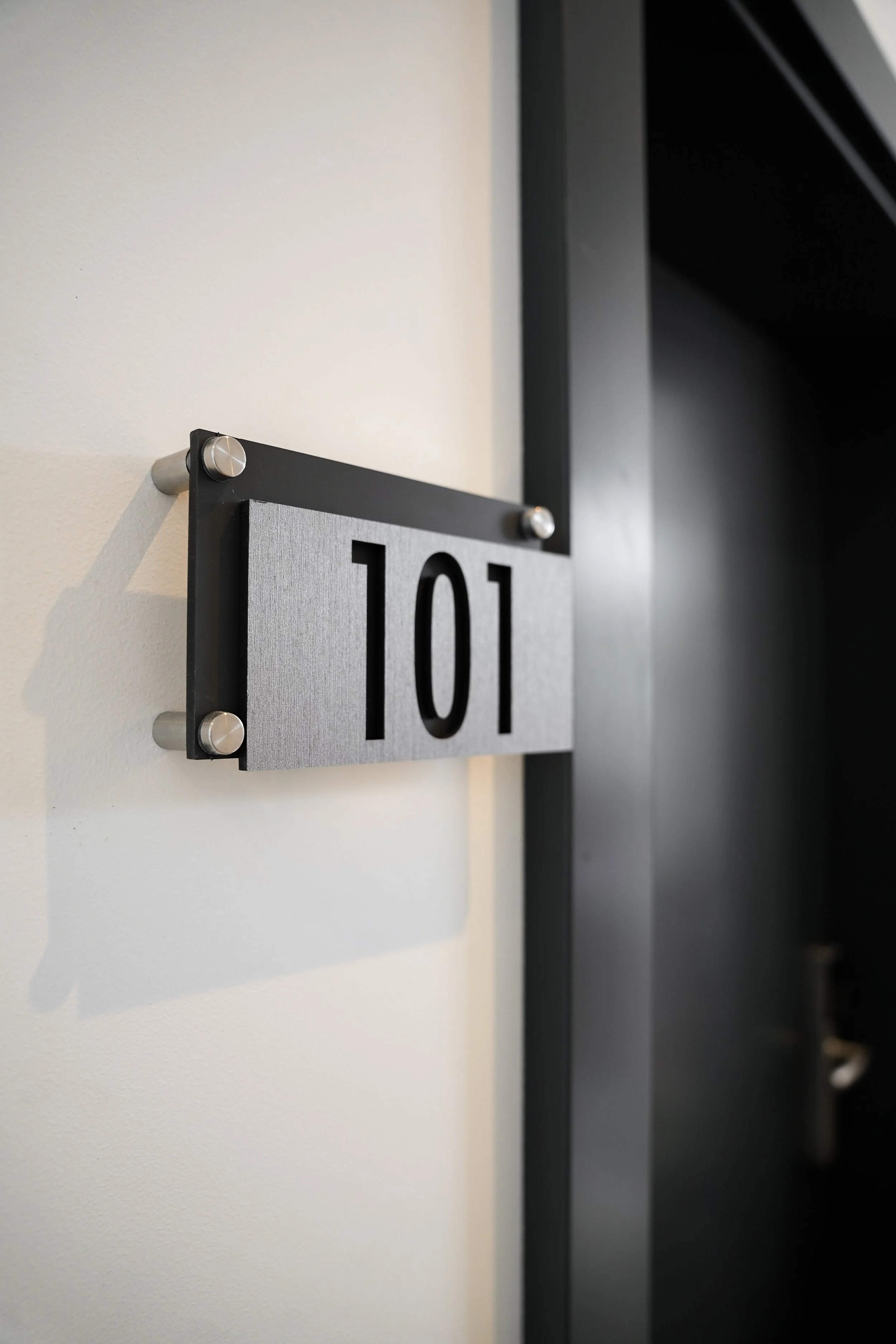 Buchstaben und nummer zeigt die Zimmernummer 101 an einem silbernen Schild an der Wand, neben einer Tür.