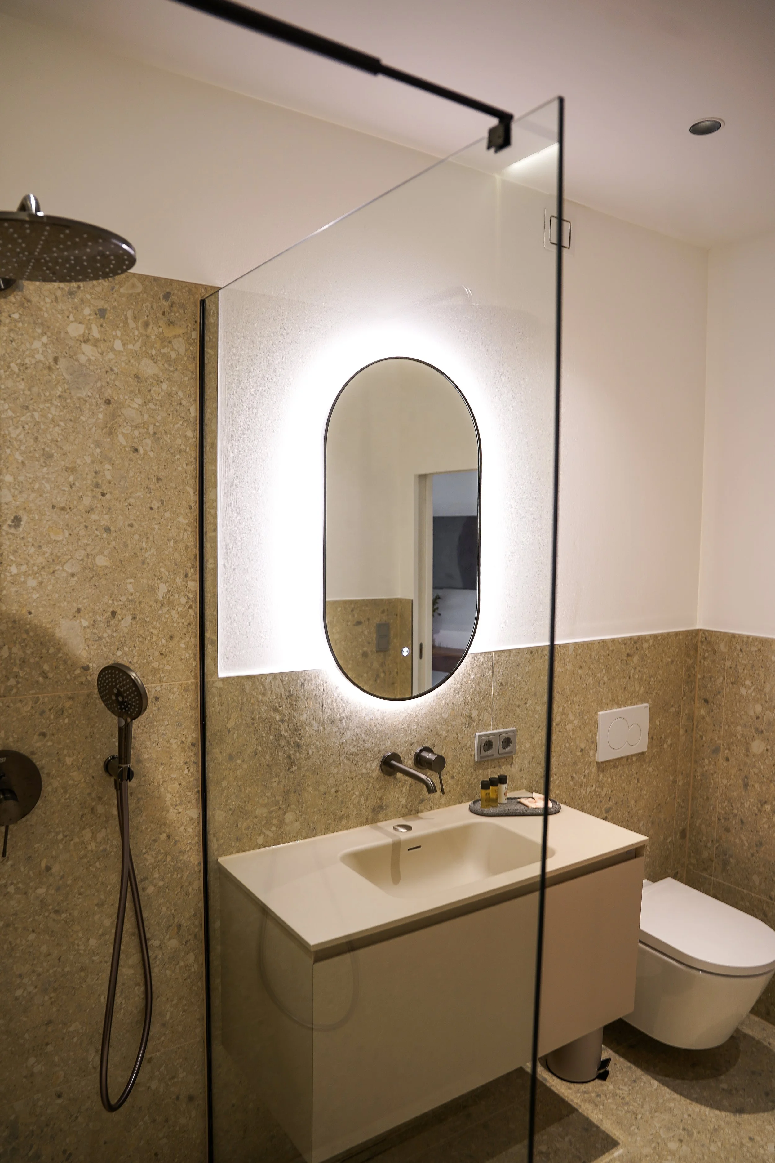 Modernes Badezimmer mit beleuchtetem Spiegel, Waschbecken, Toilette und Duschbereich mit Glaswand.