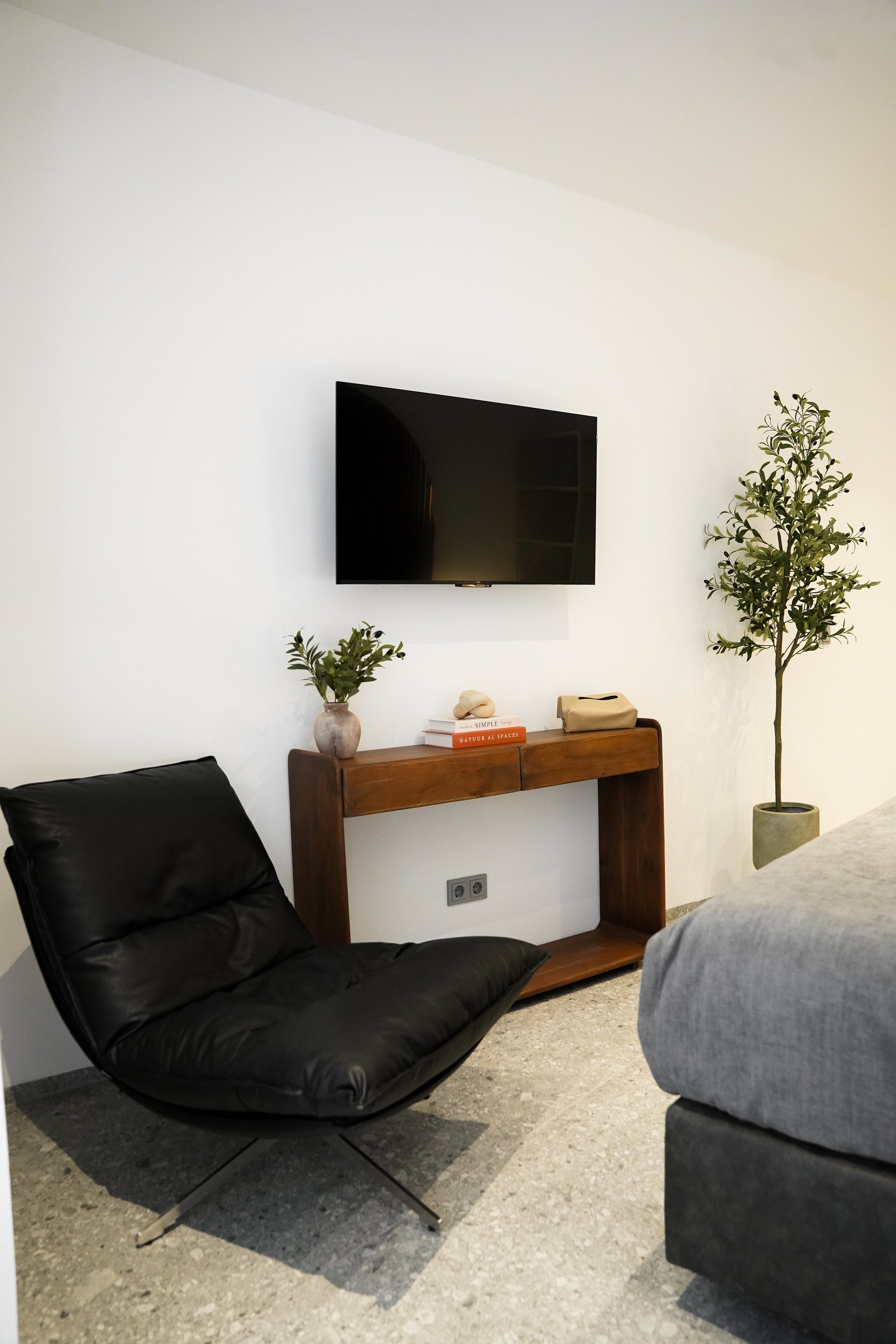 Moderner Wohnbereich mit schwarzem Sessel, Wandfernseher, Holzwandregal, Pflanzen und Dekoration