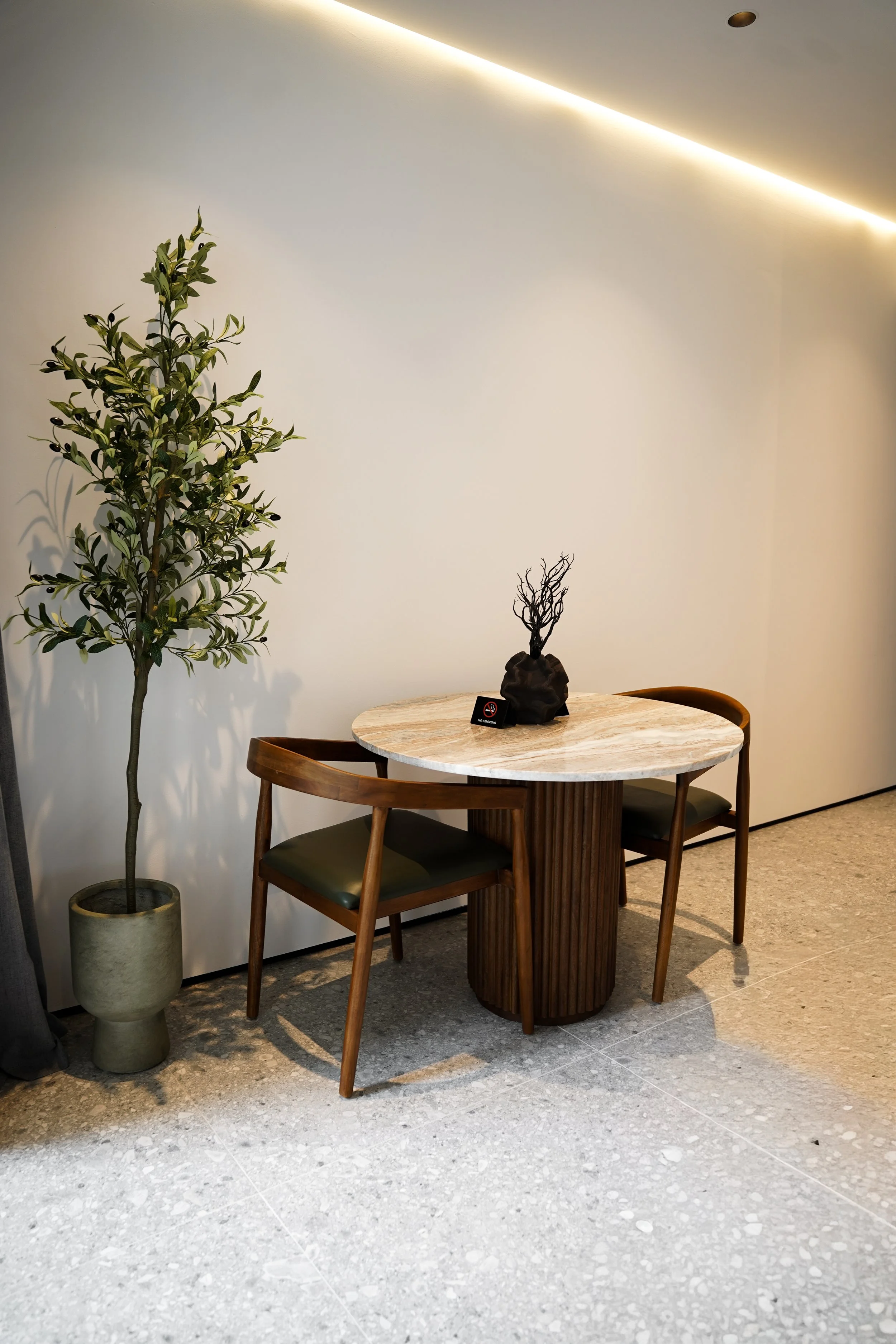 Ein runder Marmortisch mit zwei Holzstühlen, eine Topfpflanze an der Seite, eine dekorative Skulptur auf dem Tisch. Keine Personen sichtbar.