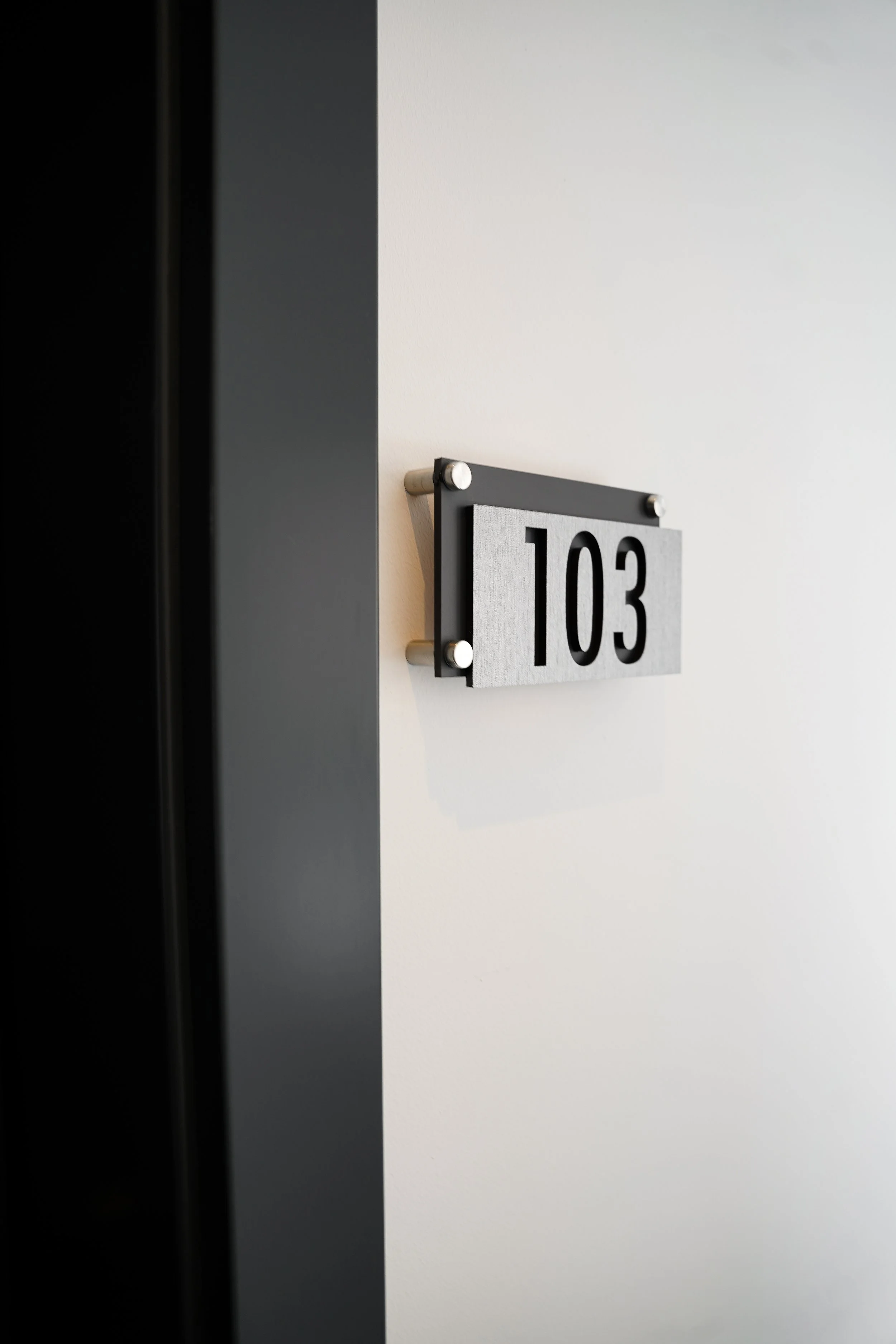 Zimmernummer 103 an einem weißen Wandstück in einem modernen Gebäude.