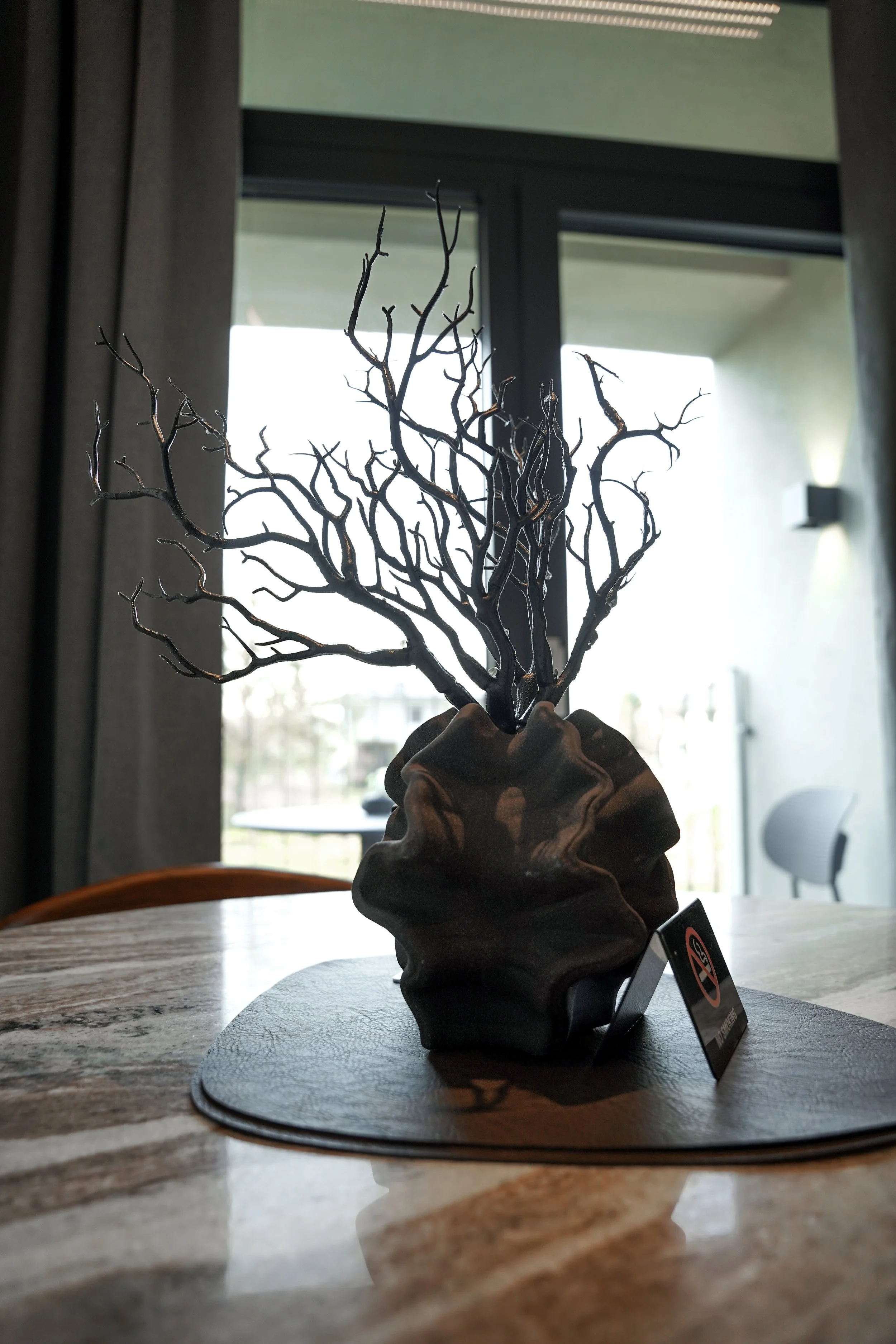 Künstliche Topfpflanze mit schwarzen Zweigen auf einem Tisch in einem Raum.