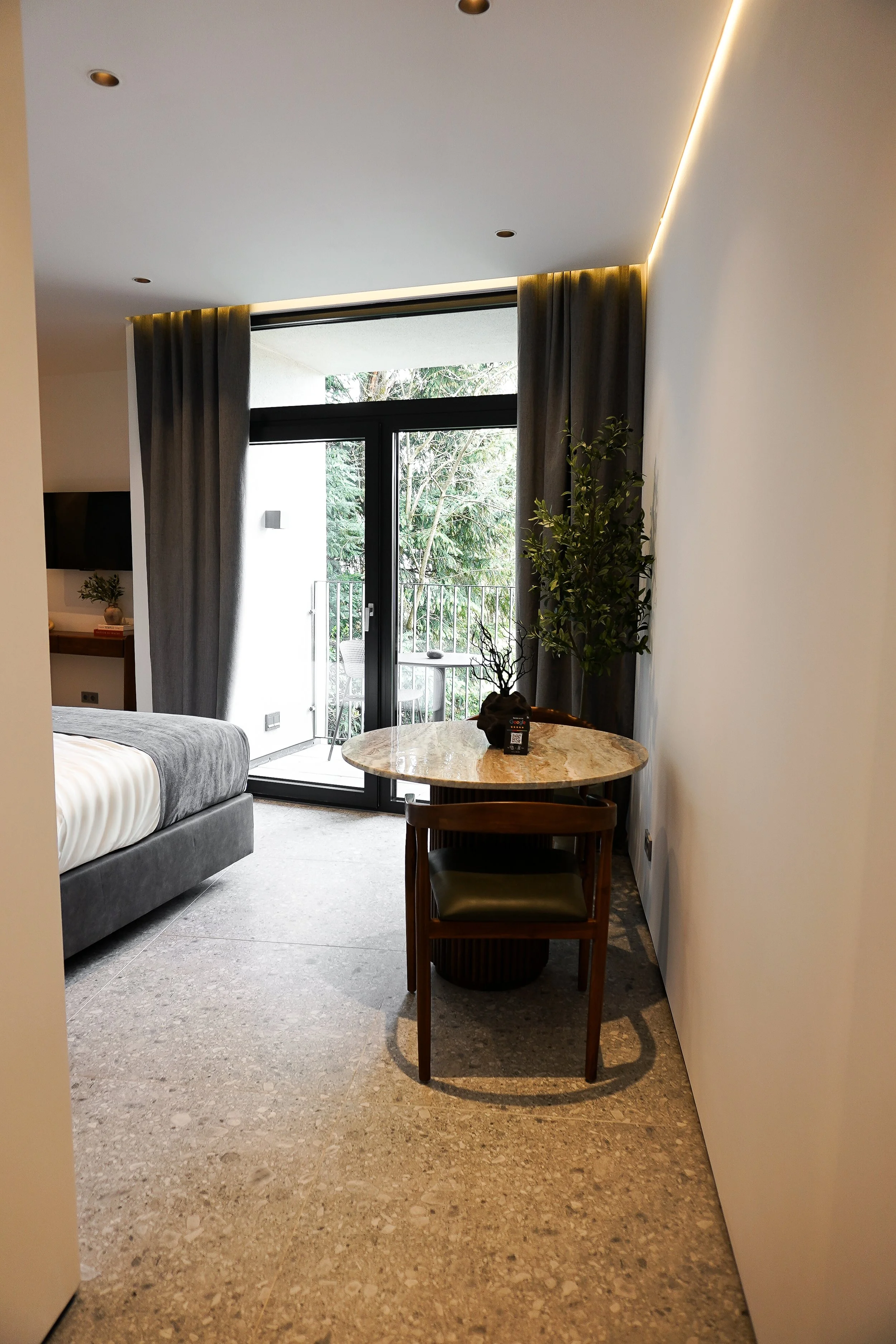 Inneneinrichtung eines Zimmers mit Balkon, eines Tisches mit Pflanze und Stuhl, Bett am linken Rand, große Fenster mit Vorhängen, moderner Stil.