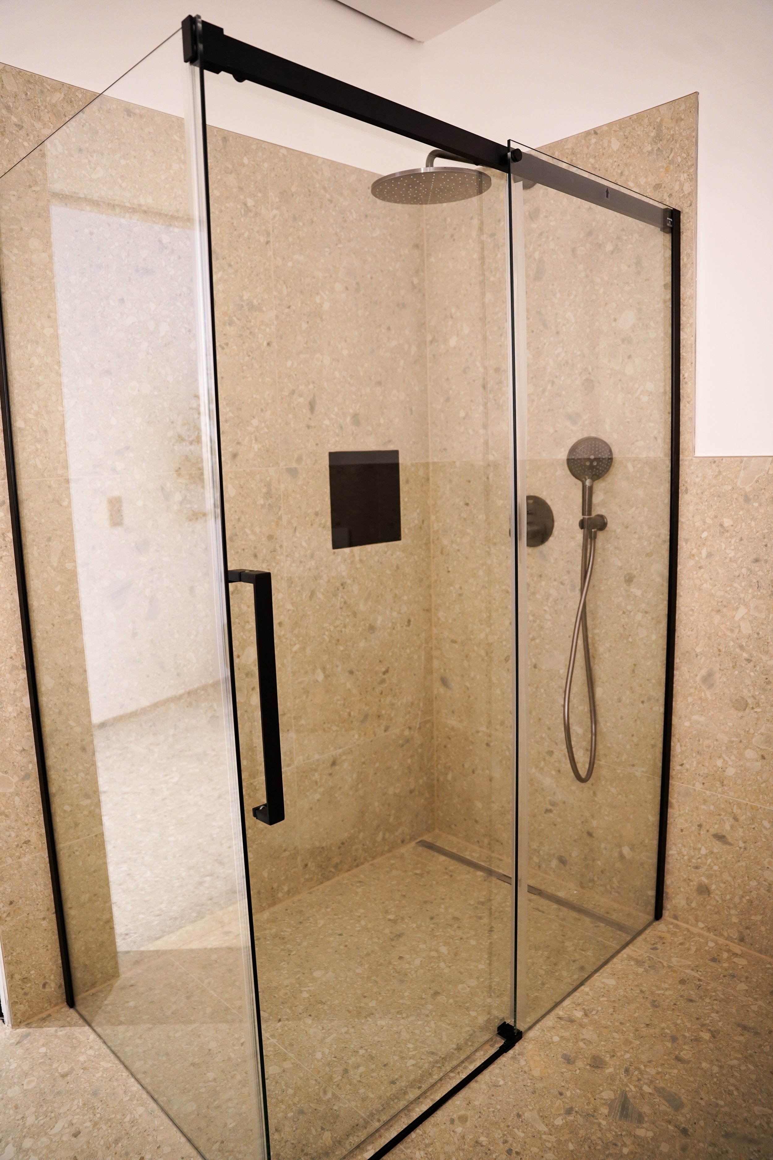 Moderne begehbare Dusche mit Glaswänden und schwarzem Track-System, beige Fliesen