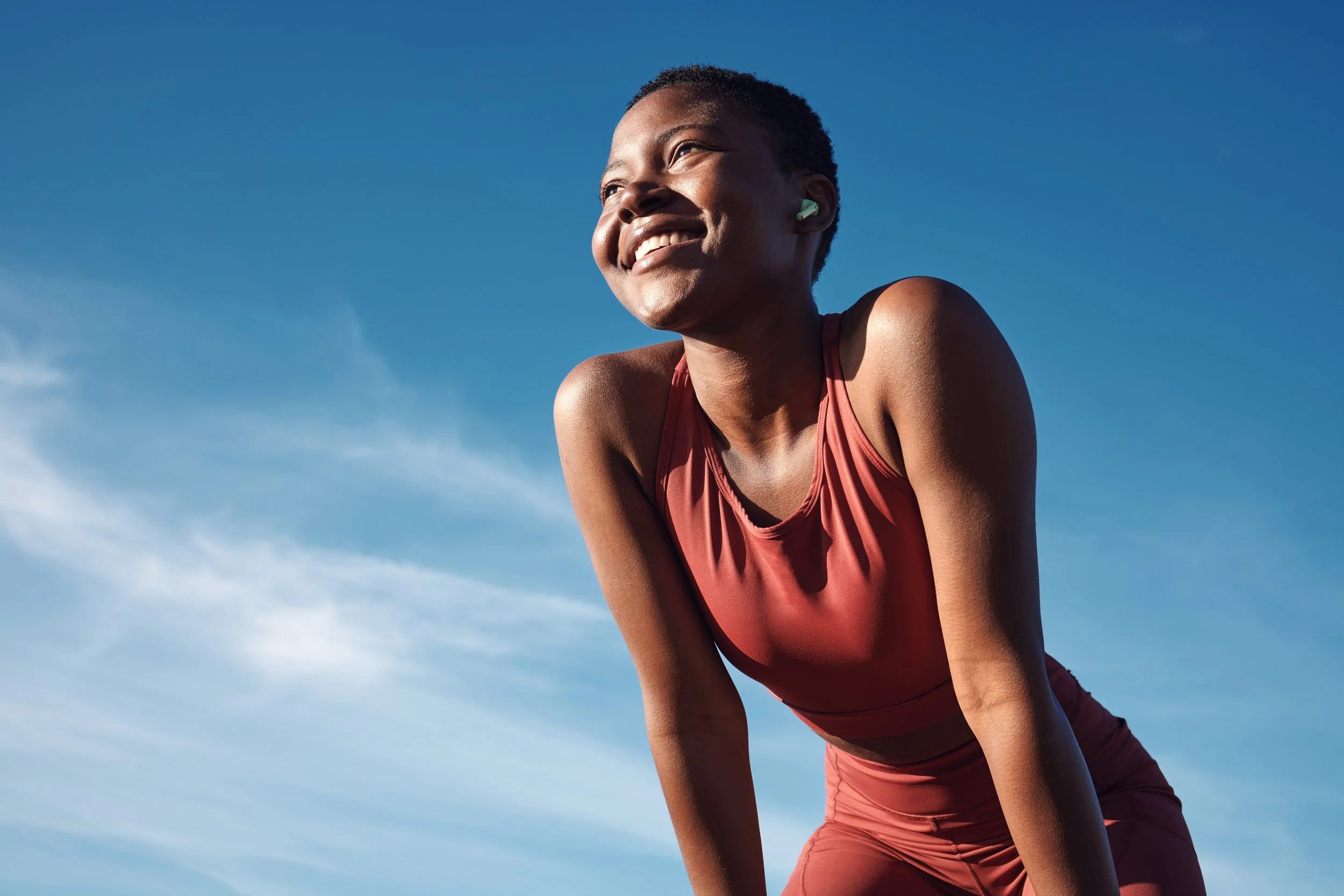 An athletic young woman in athletic wear smiling outdoors against a blue sky.